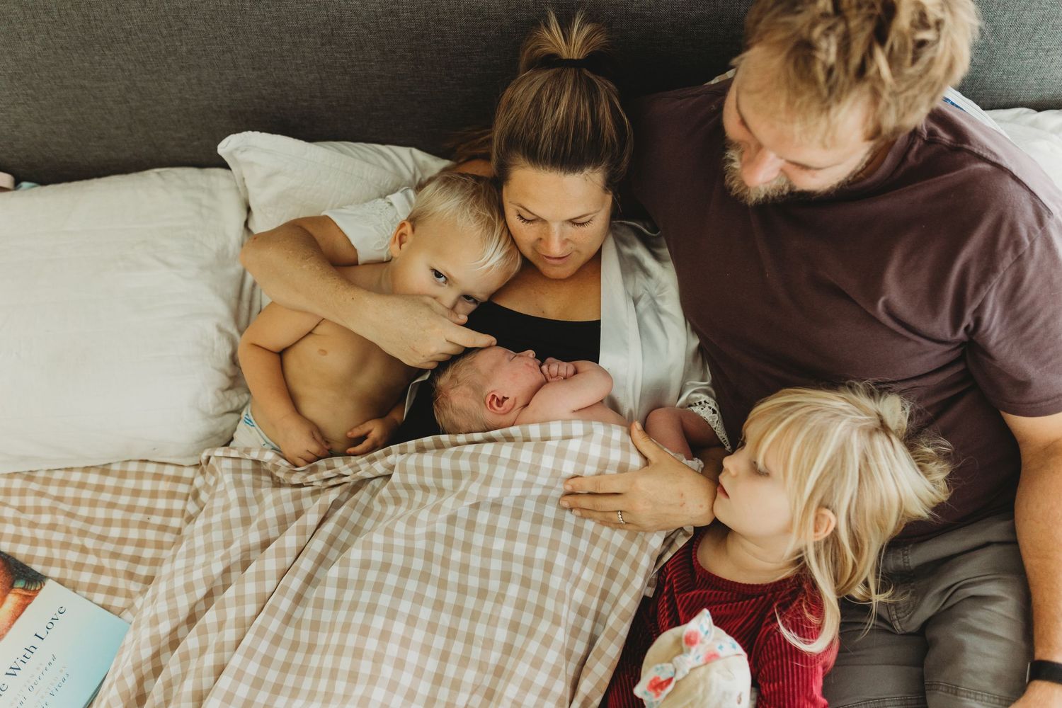 Family of four with newborn baby cuddling together on bed during fresh 48 session.