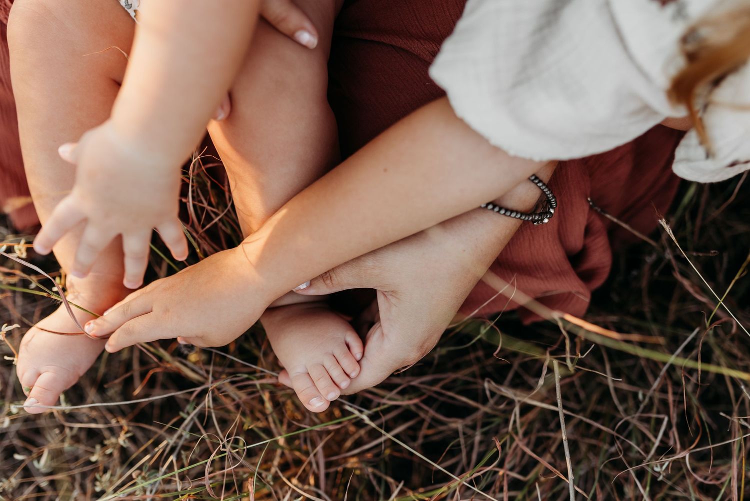 Close-up of bare feet of mother and young children sitting in dry grass.