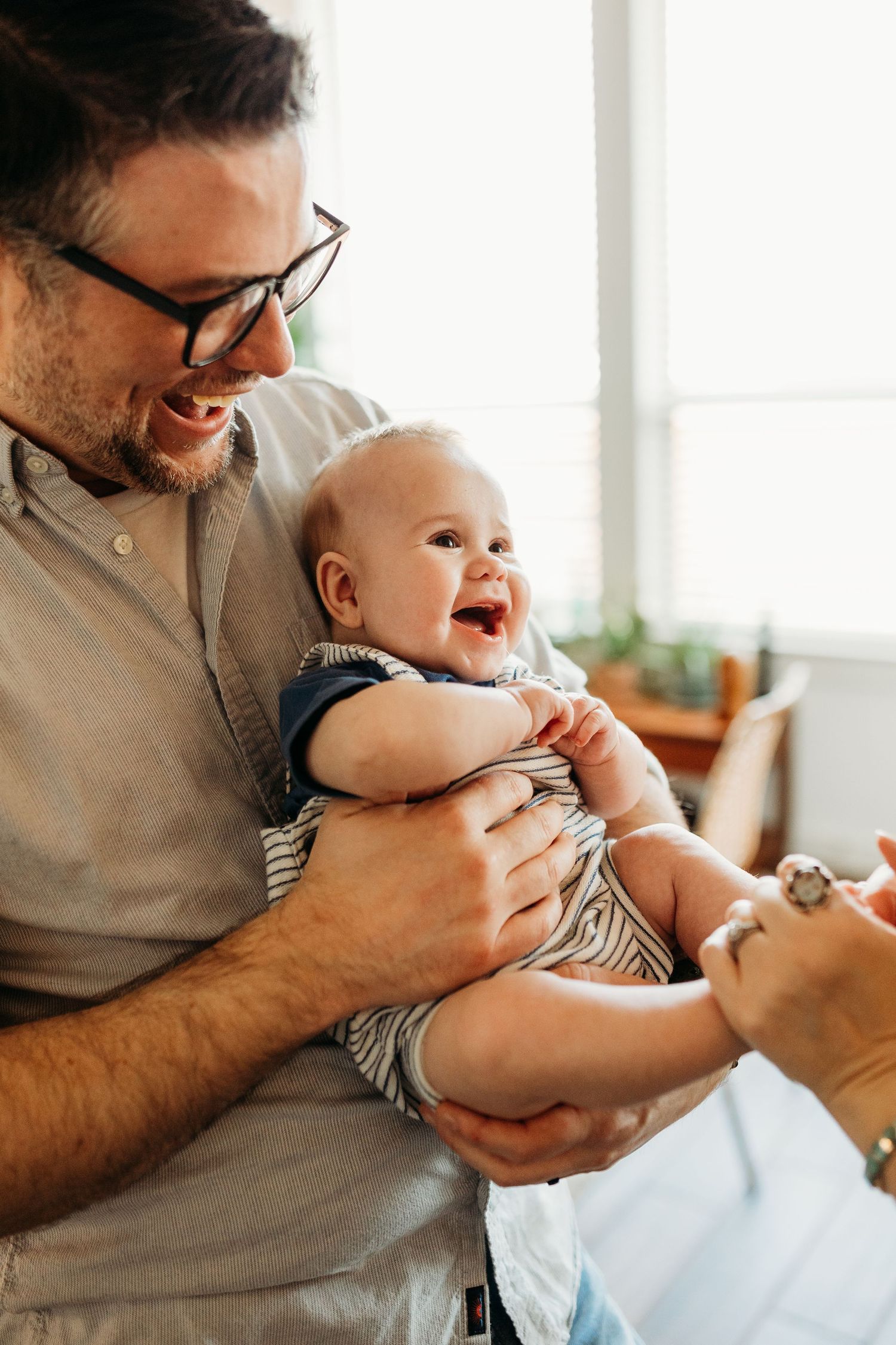 Laughing baby held by smiling father with glasses in bright home setting.