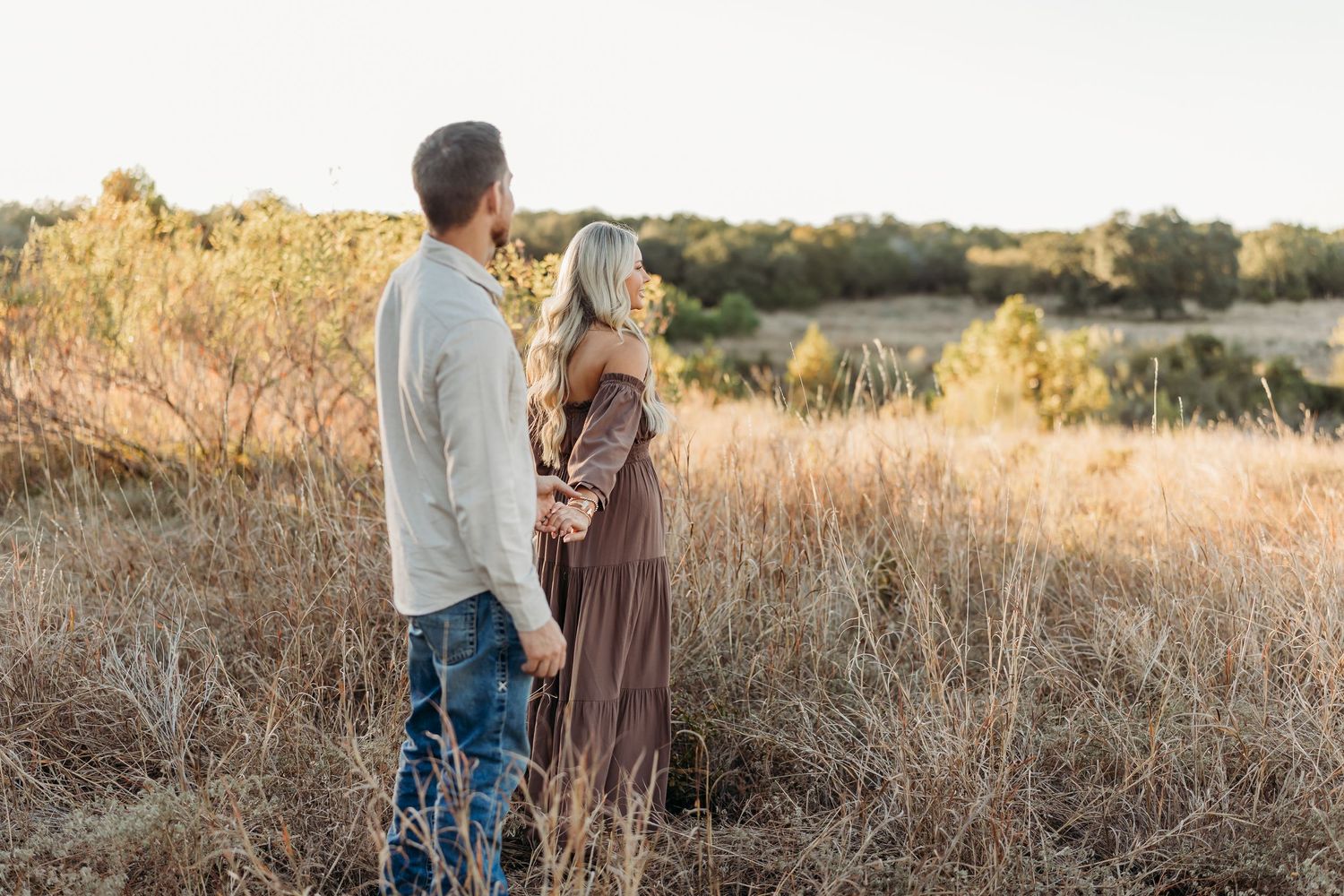 Couple holding hands and gazing at each other in a golden field at sunset.