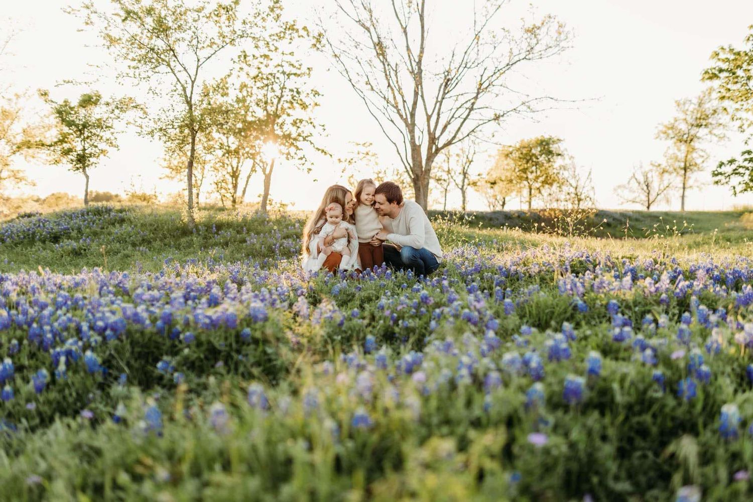 A family sits together in a field of blooming bluebonnets at golden hour.