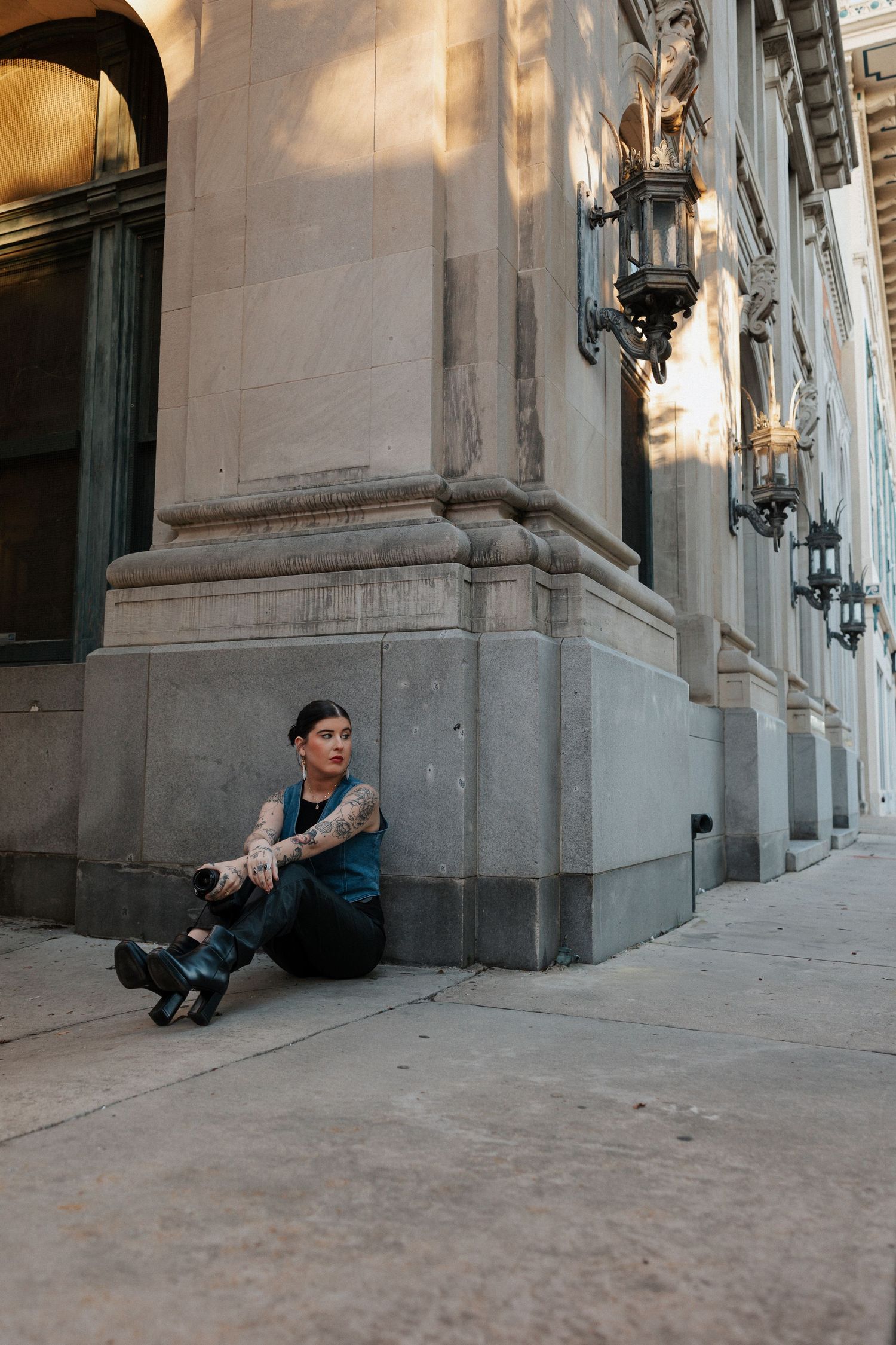 photographer, sitting on ground, back against wall, looking away, girl holding camera, tattoos