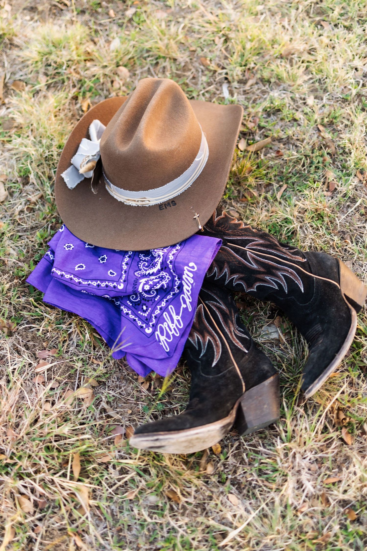 Brown cowboy hat, purple bandana, and black western boots arranged on grass.