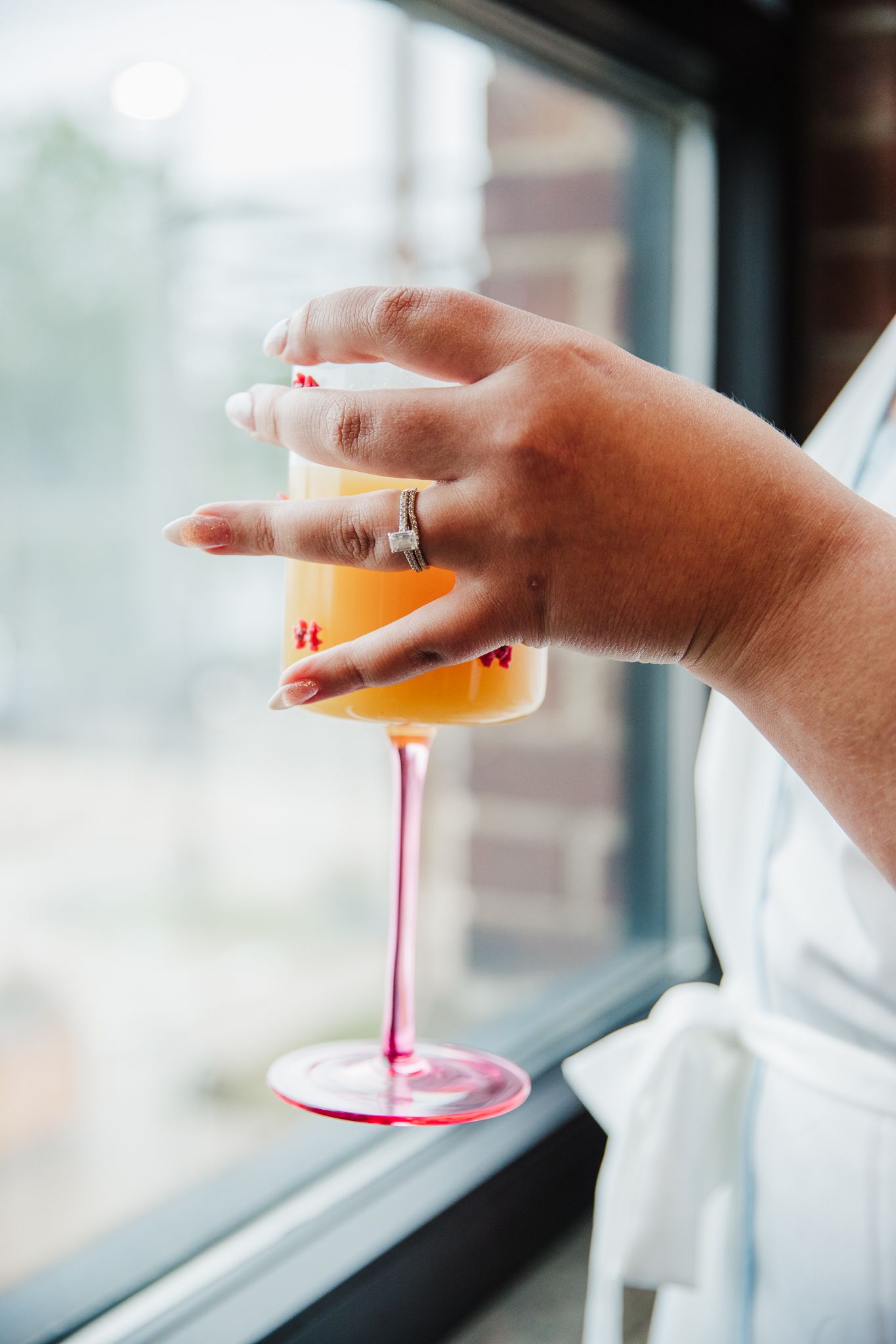 Hand holding a champagne cocktail in a stemmed glass against a window backdrop.