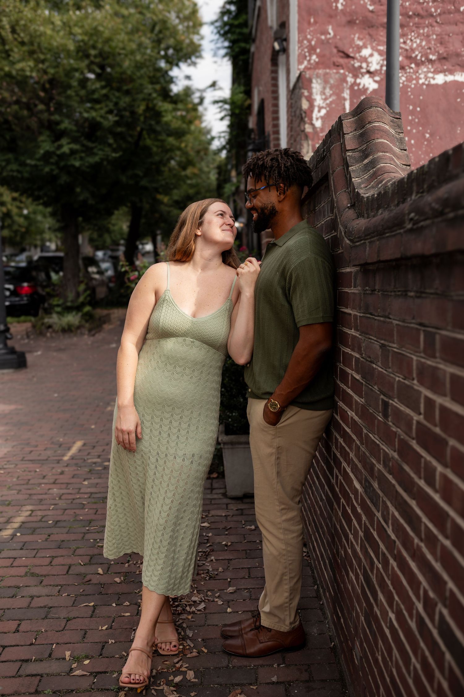 A couple shares an intimate moment on a brick-lined street beside an old red brick building.