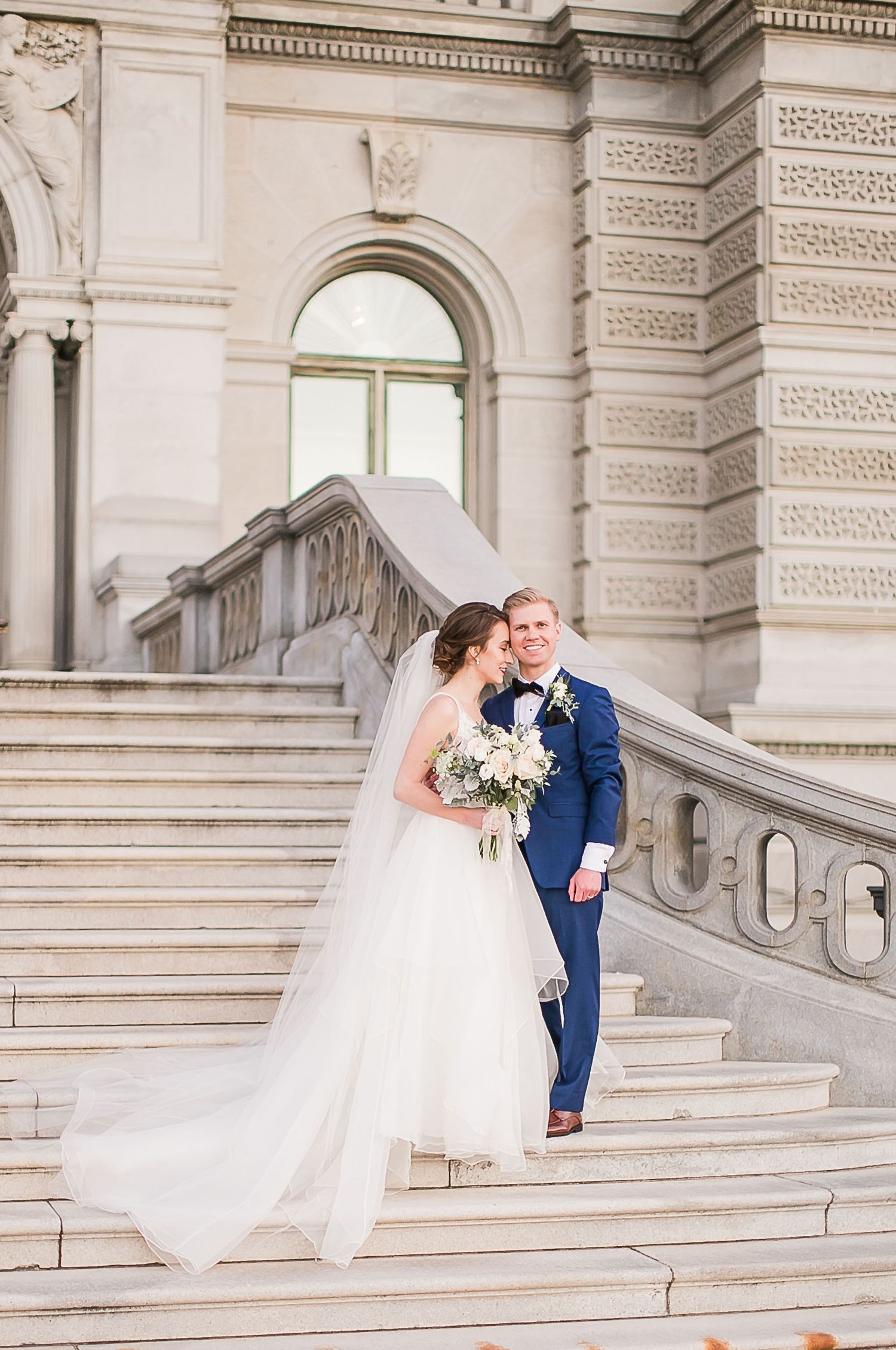 Elegant white stone staircase with ornate architectural details at historic venue decorated for wedding ceremony.