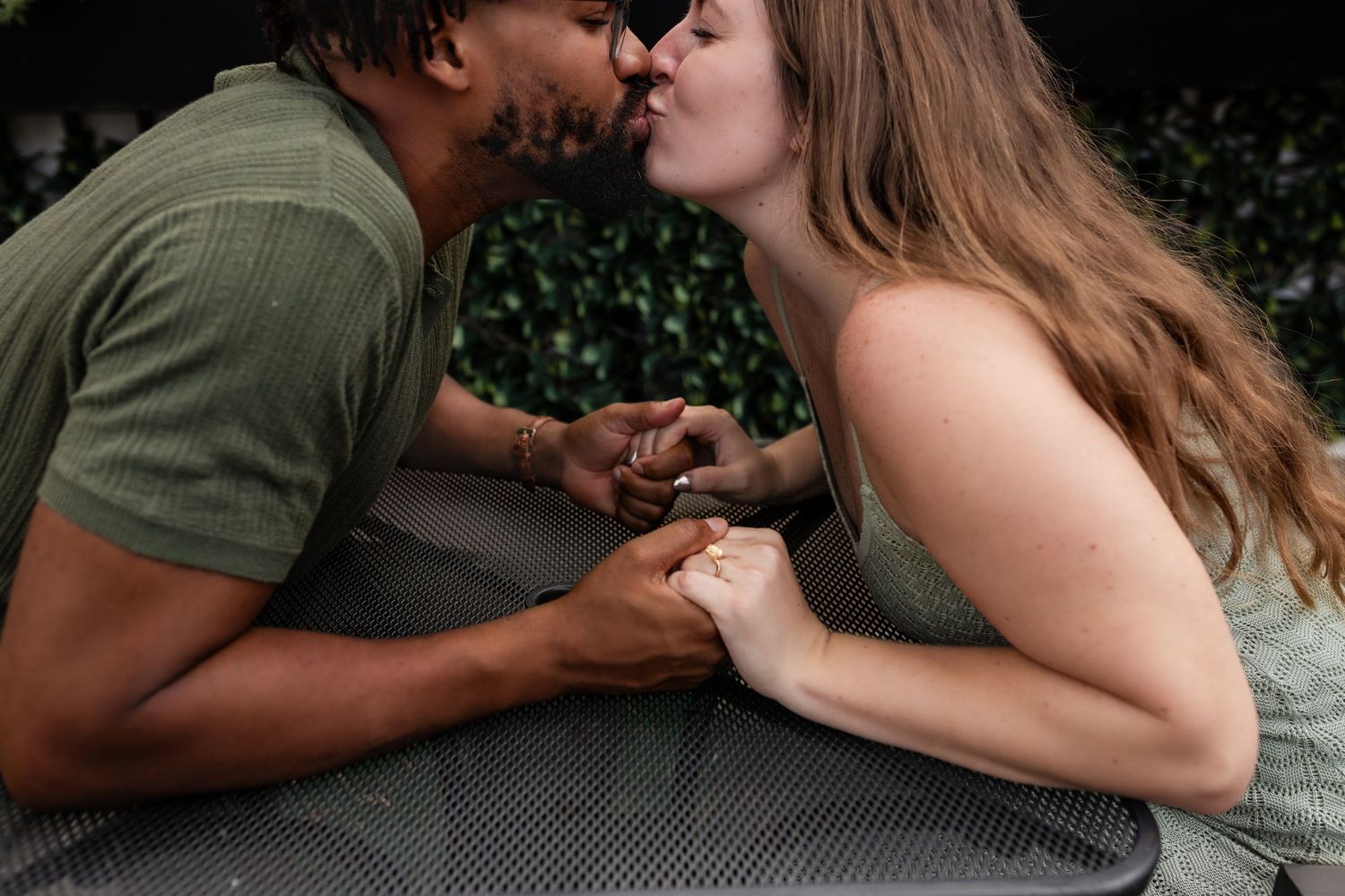 Close-up shot of a romantic couple holding hands and sharing an intimate moment against a green leaf background.