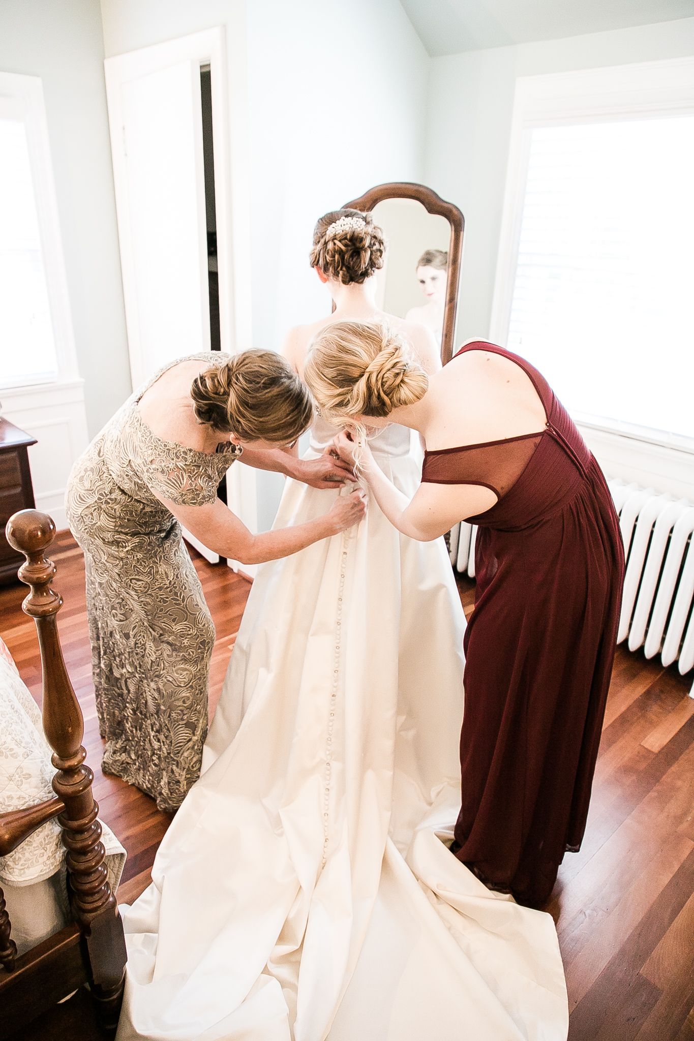 A group of women helps dress a bride in her white wedding gown during preparation for her special day.