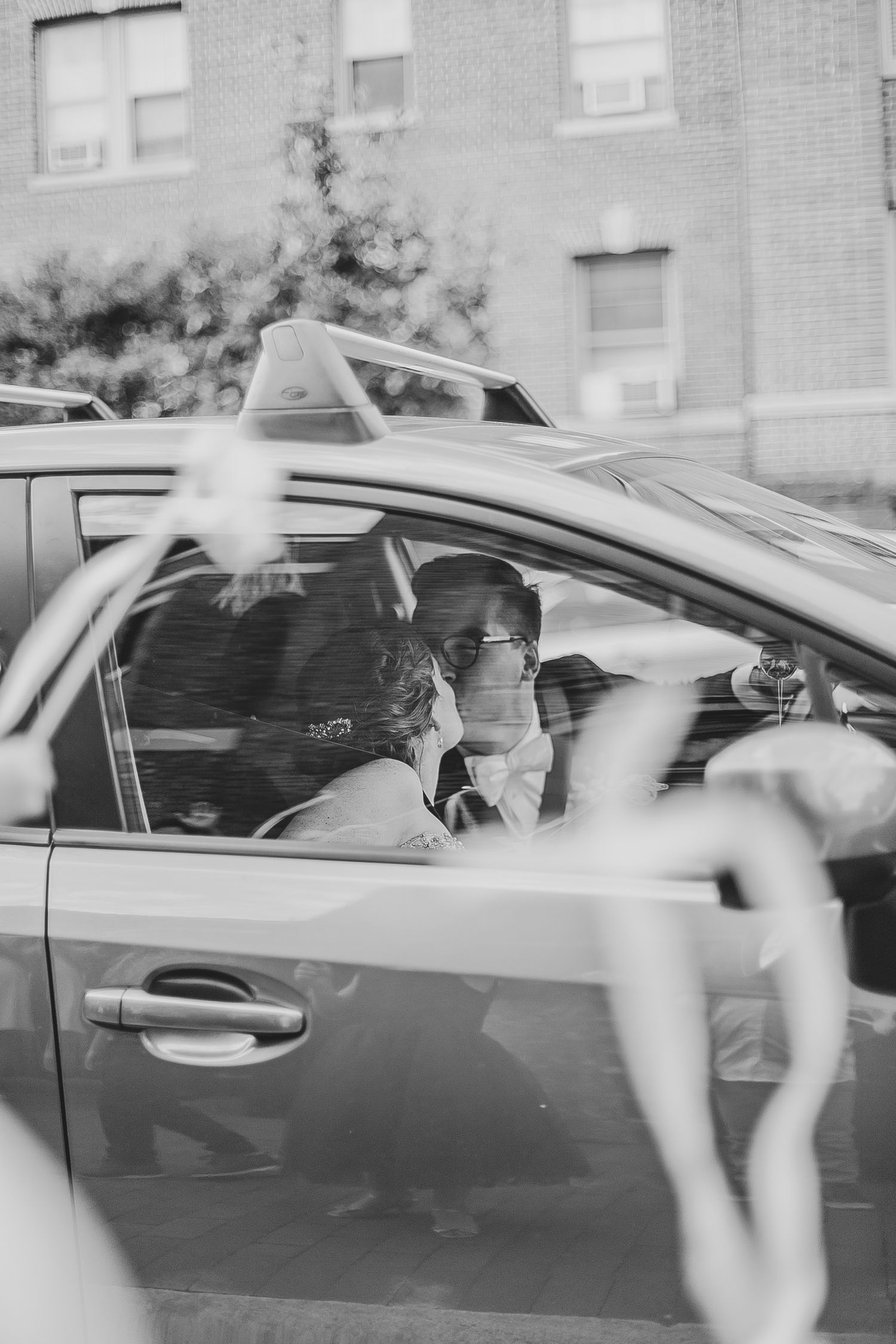 Multiple black and white photographs showing blurry motion of cars with people inside them on a brick building background.