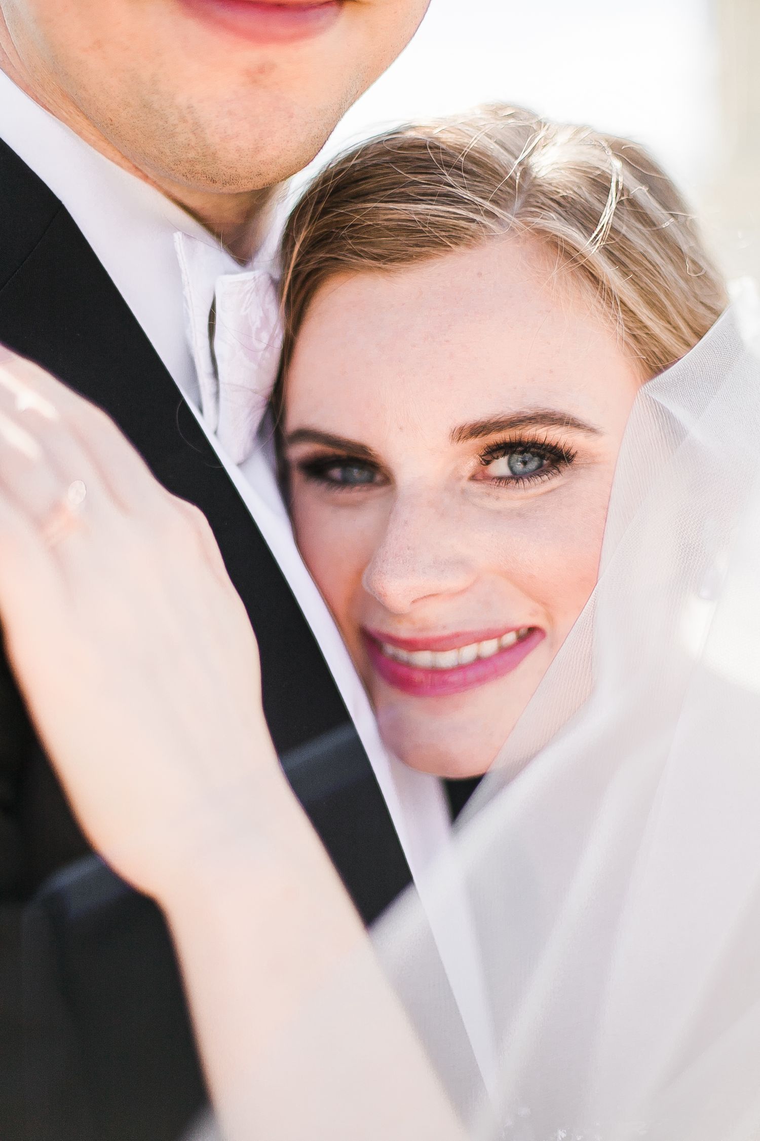 A joyful bride with sparkling eyes and a radiant smile peeks out from behind her new spouse on their wedding day.