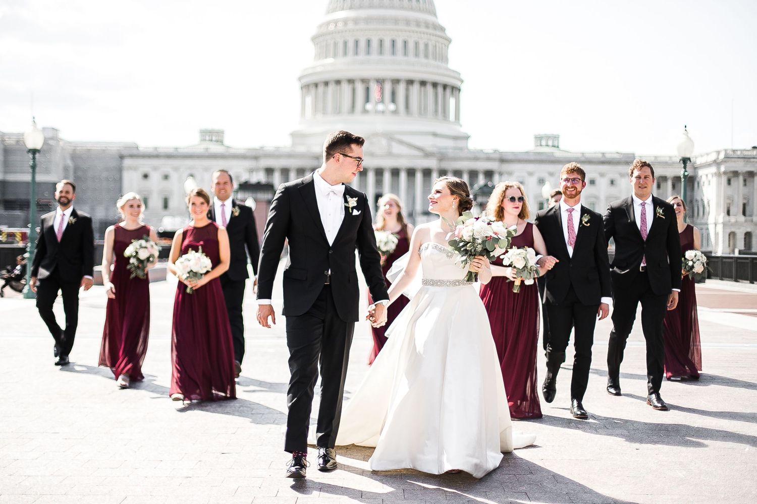 A wedding party in black suits and burgundy dresses poses in front of the US Capitol Building in Washington, DC.