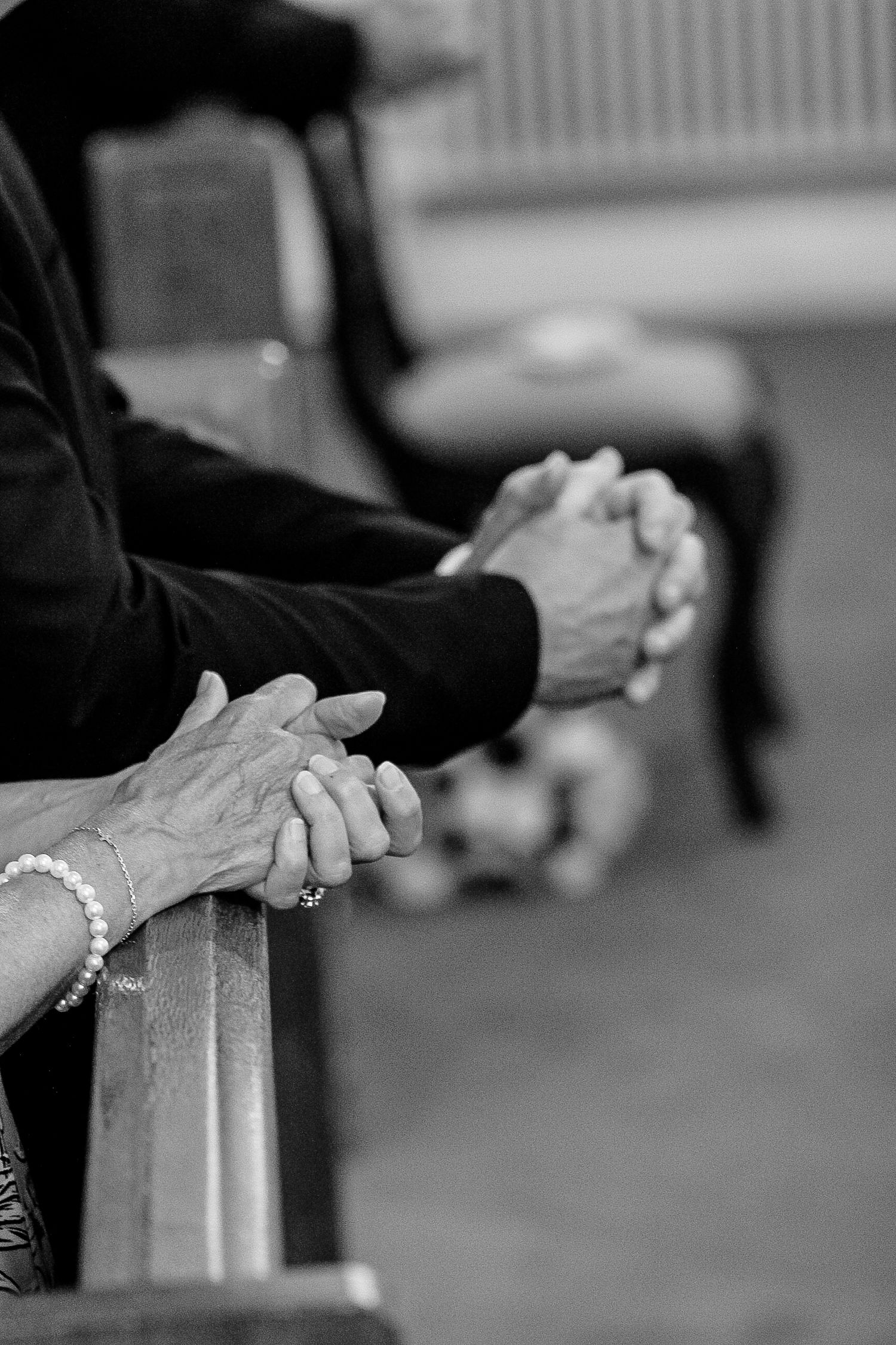Black and white image showing clasped hands resting on a railing during what appears to be a church service.