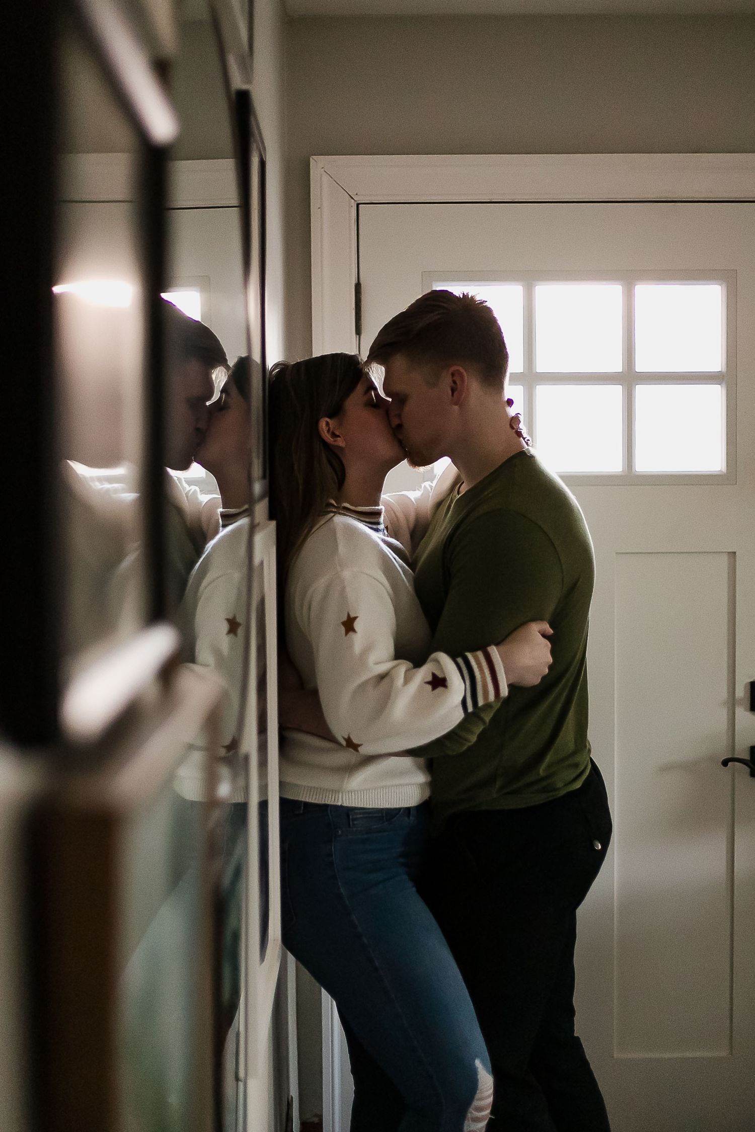 A romantic couple embraces in a dimly lit hallway against a white door, creating an intimate moment at home.