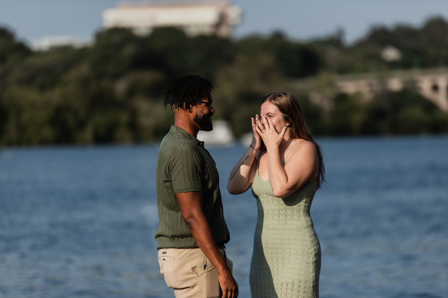 A couple embraces while standing near a scenic lake in golden light.