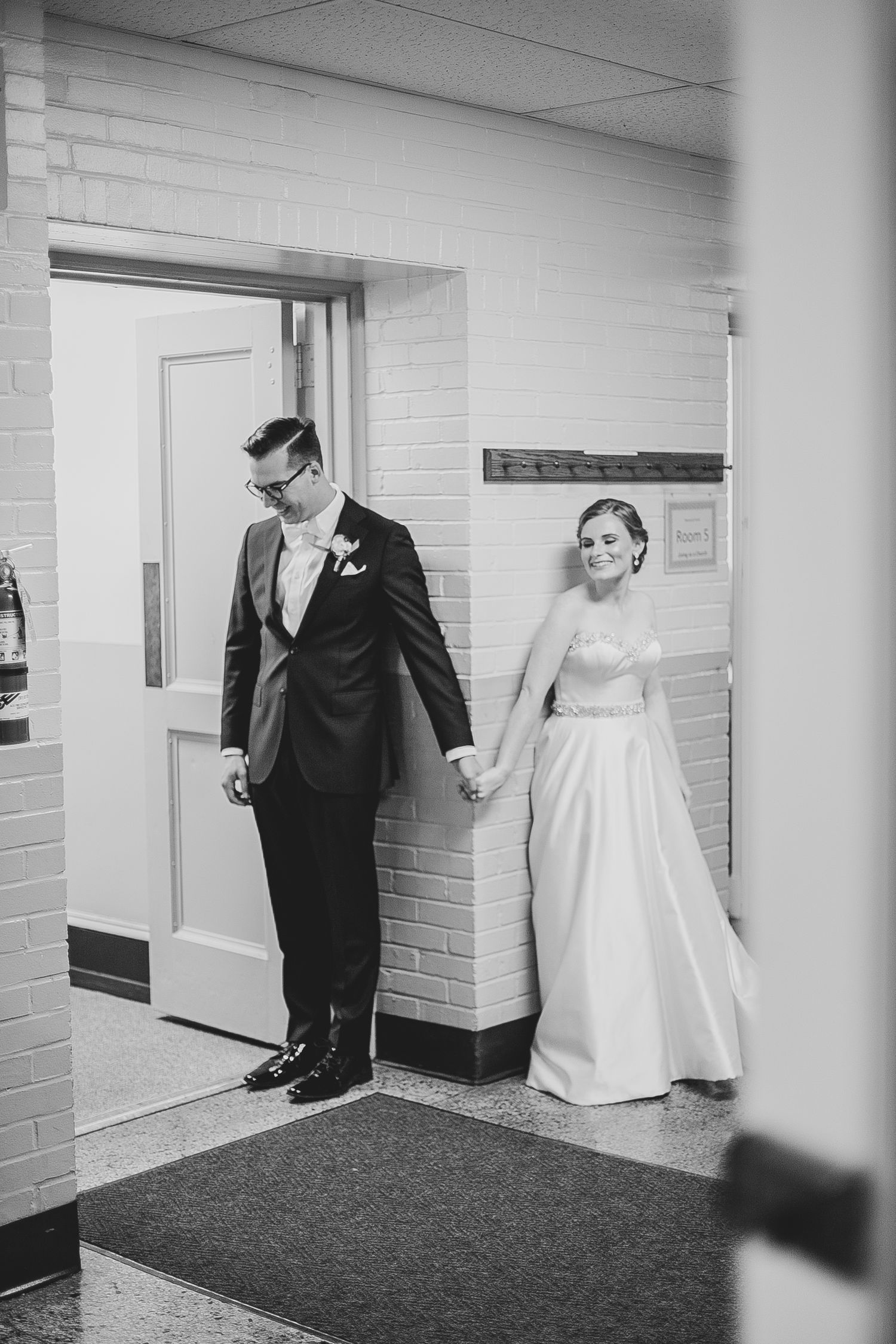 A black and white photo of a bride and groom holding hands around a corner at their wedding.