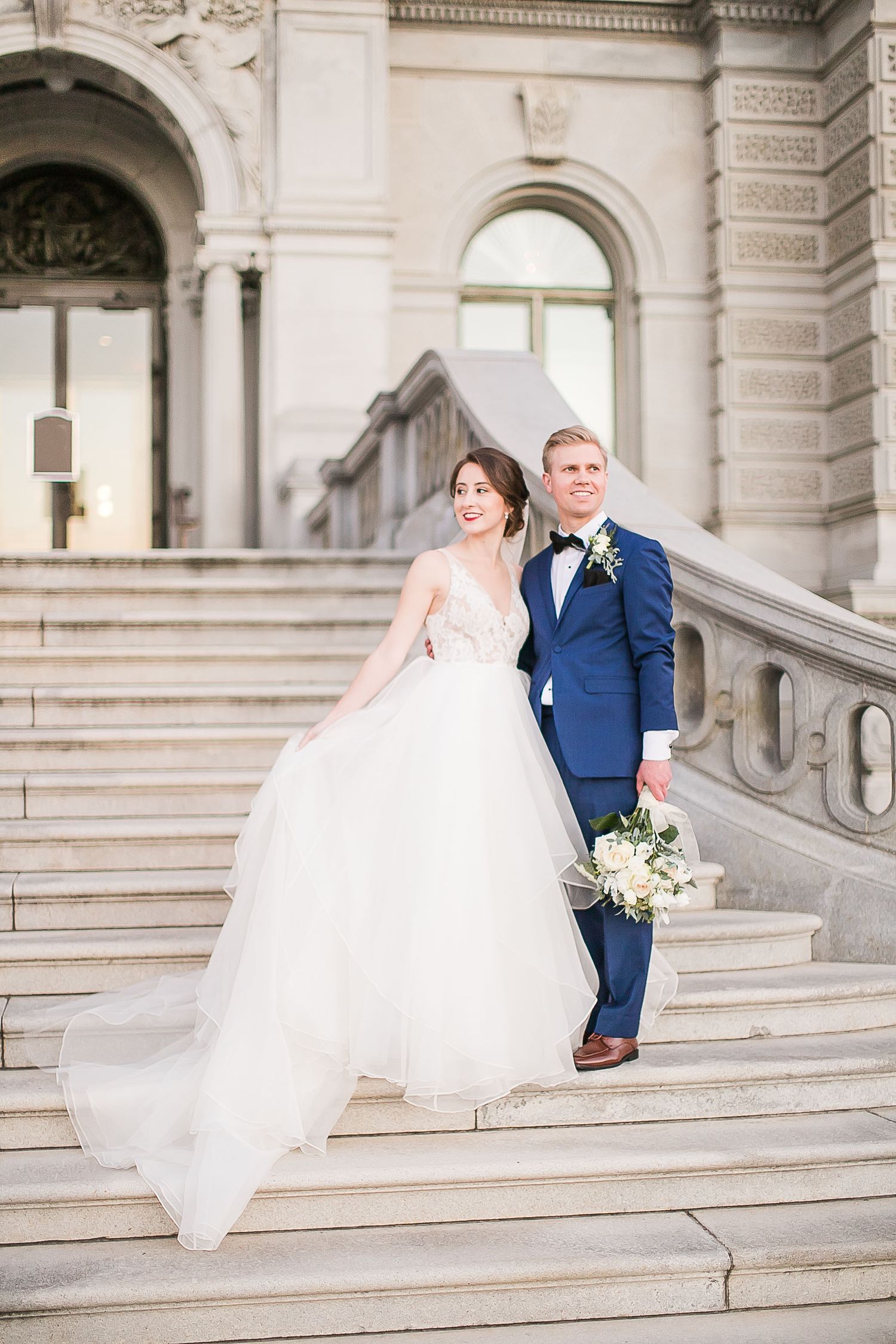 Elegant wedding couple posing on grand stone steps of historic building in classic architectural setting.