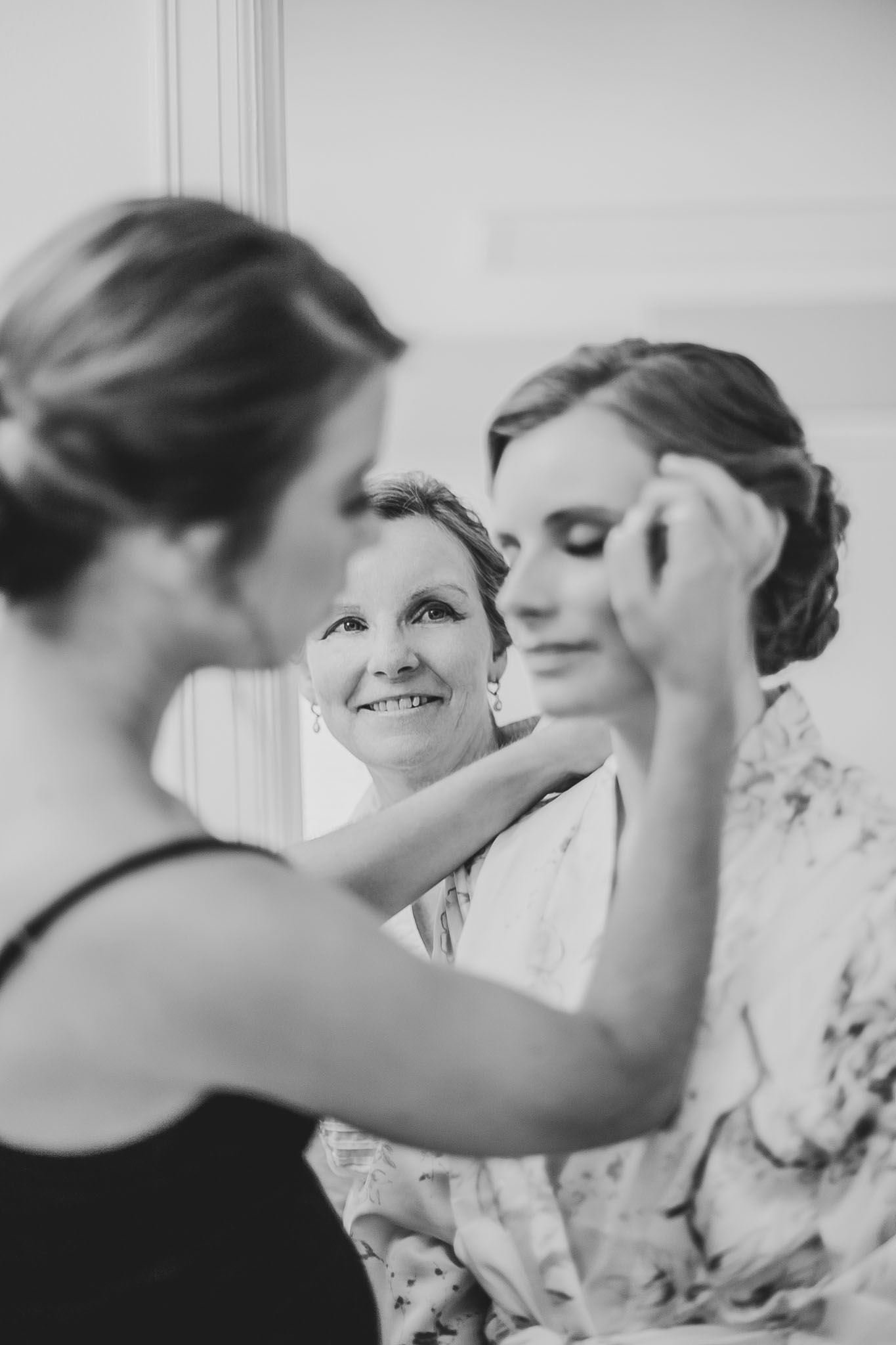 Black and white candid photo of tender bridal preparations showing joyful interaction between women getting ready.