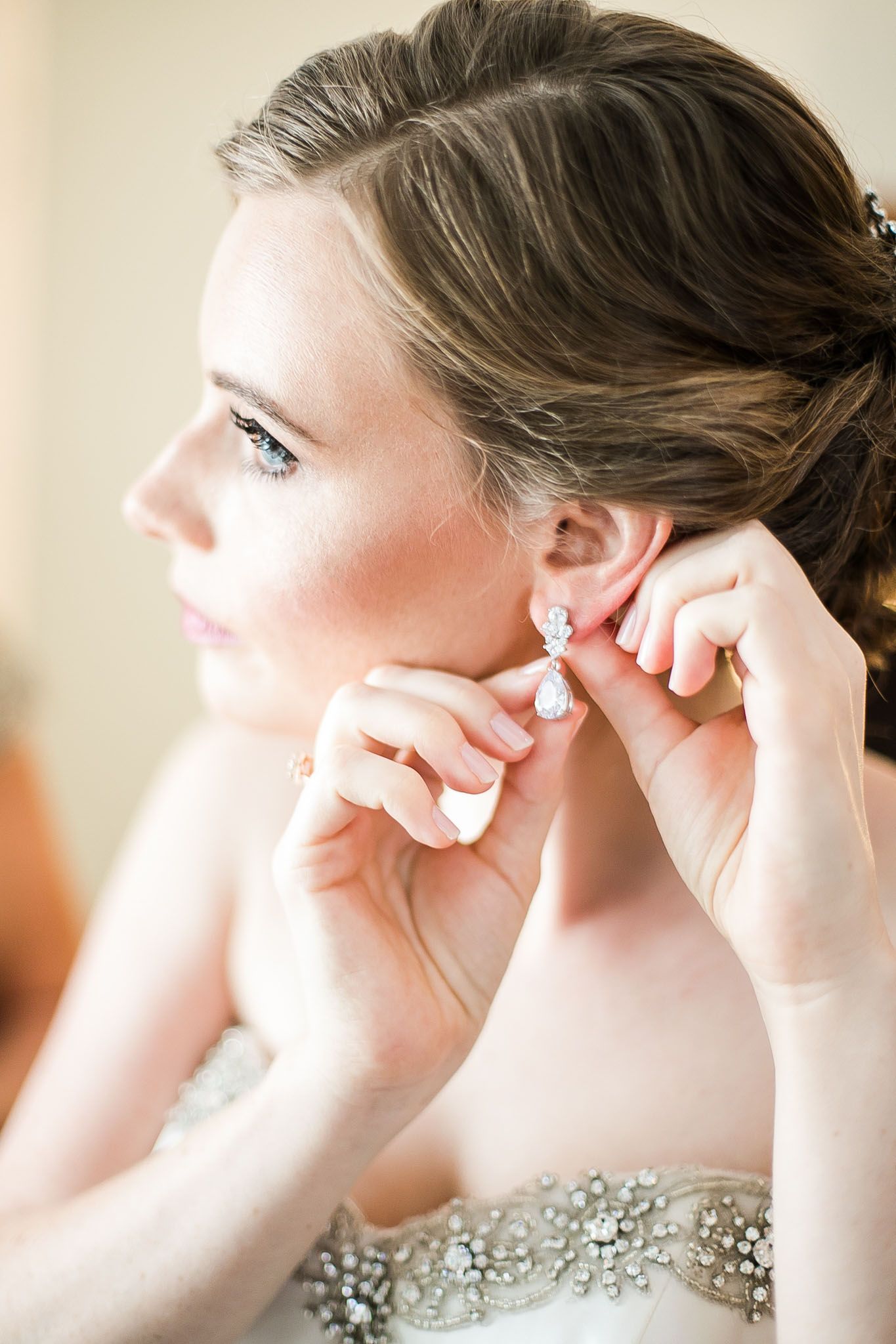 Side profile of someone putting on an earring while wearing a strapless dress with crystal embellishments.