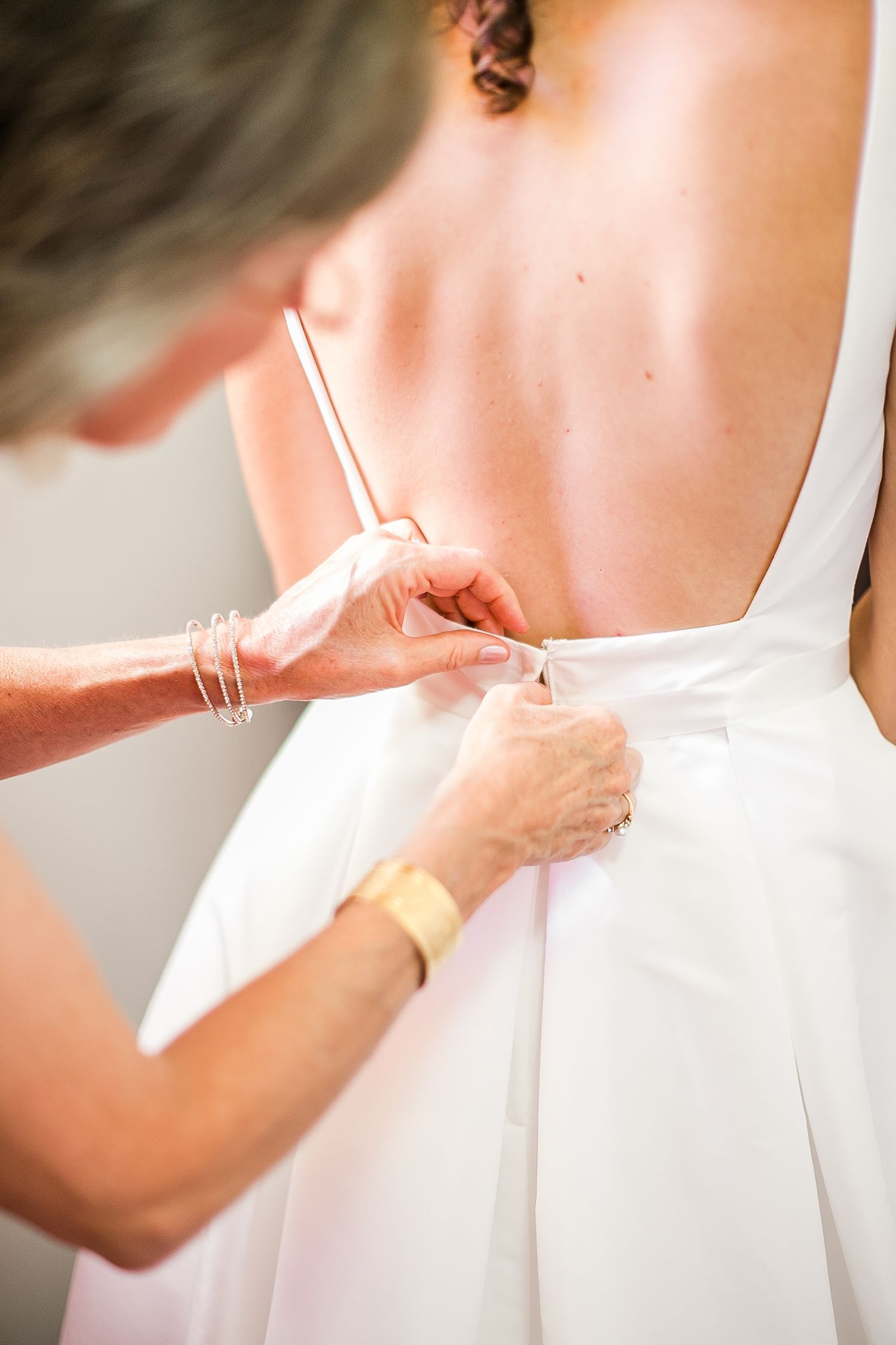 Someone helps fasten the buttons or clasps on the back of an elegant white wedding dress during final preparations.