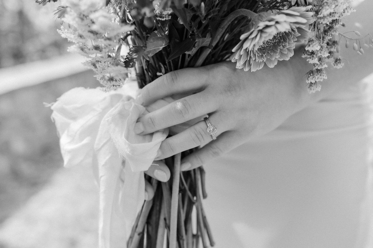 A close-up view of a wedding bouquet with blush pink and white flowers wrapped in a satin ribbon.