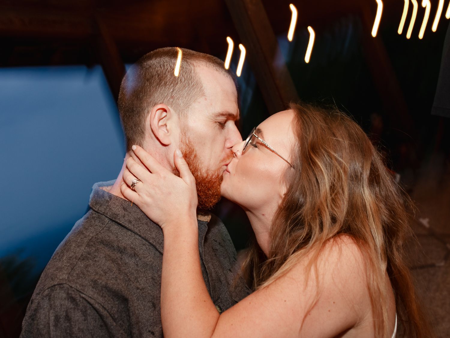 A romantic couple shares a tender kiss during an evening moment together with blurred lights in the background.