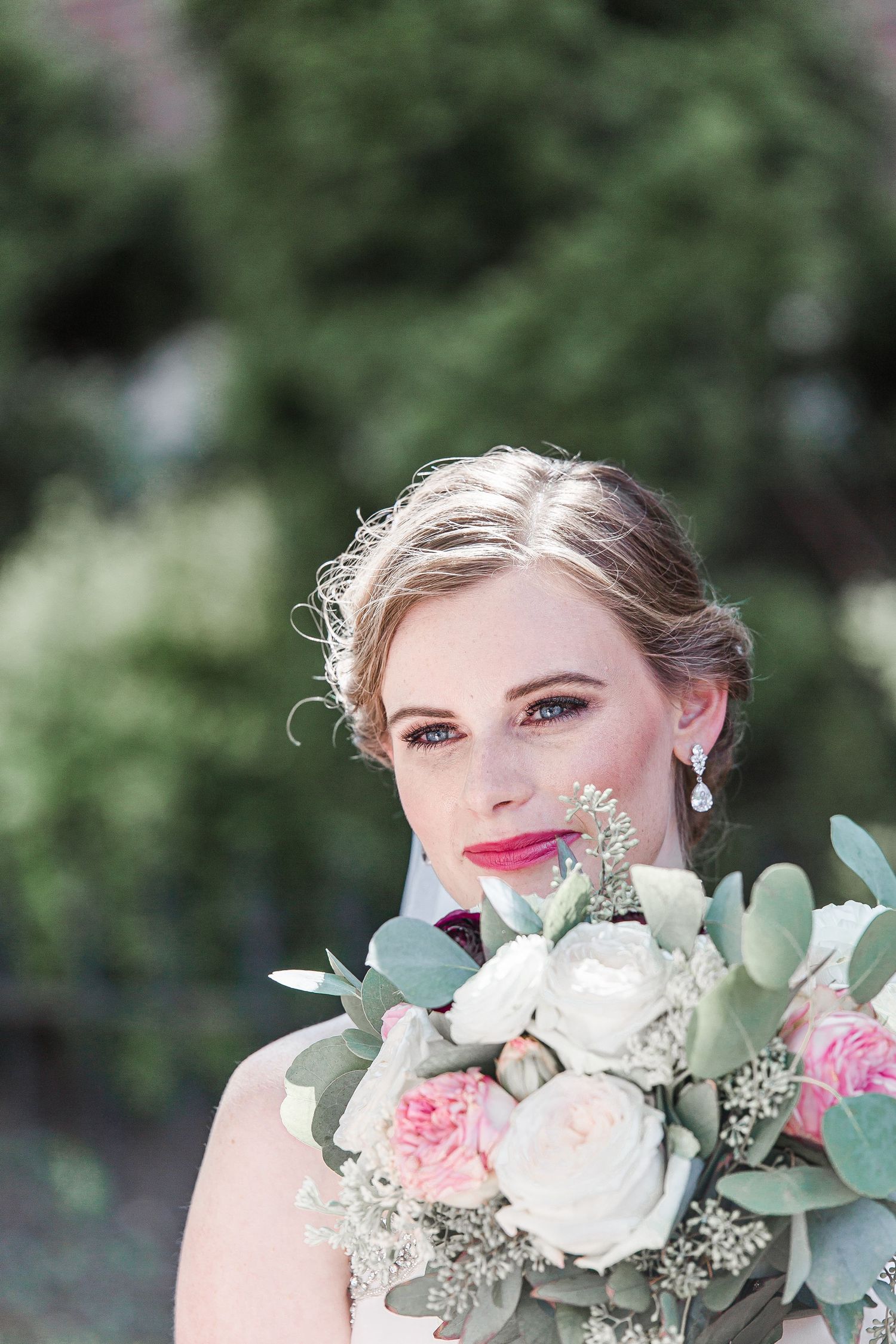 A romantic bridal portrait features a delicate bouquet of pink and white roses with eucalyptus against a soft blurred background.