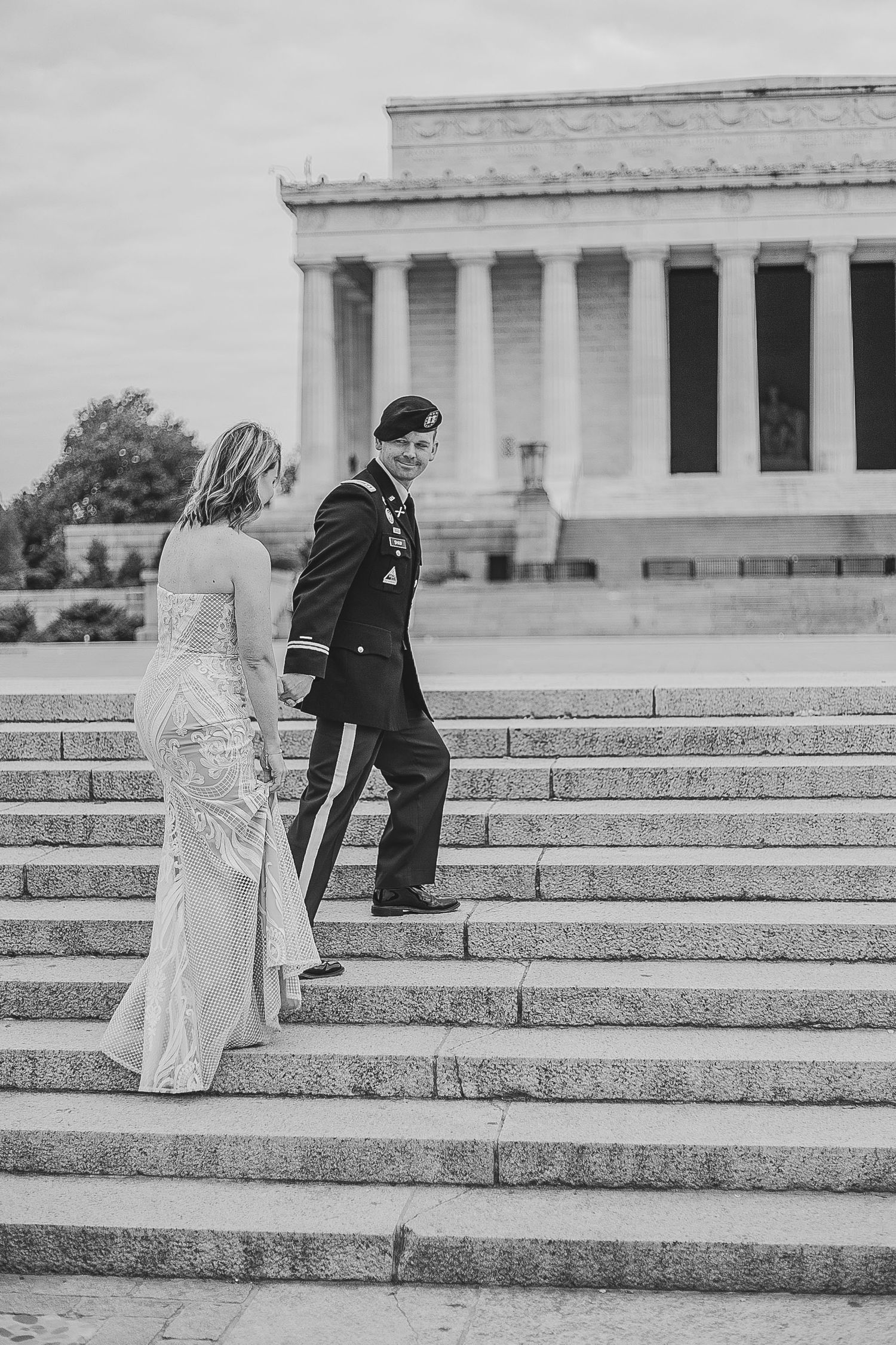 A couple in formal wedding attire ascends the steps of the Lincoln Memorial in Washington DC in black and white.