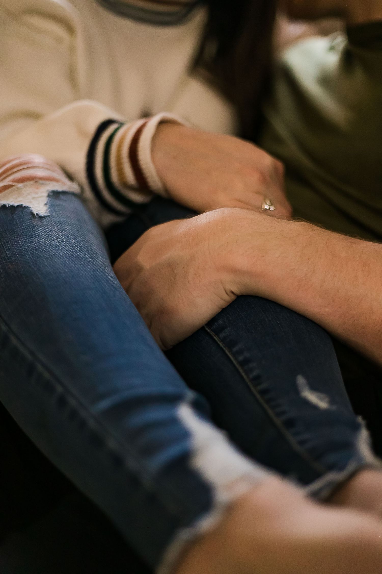 Close-up view of people holding hands on ripped denim jeans showing an intimate moment of connection.