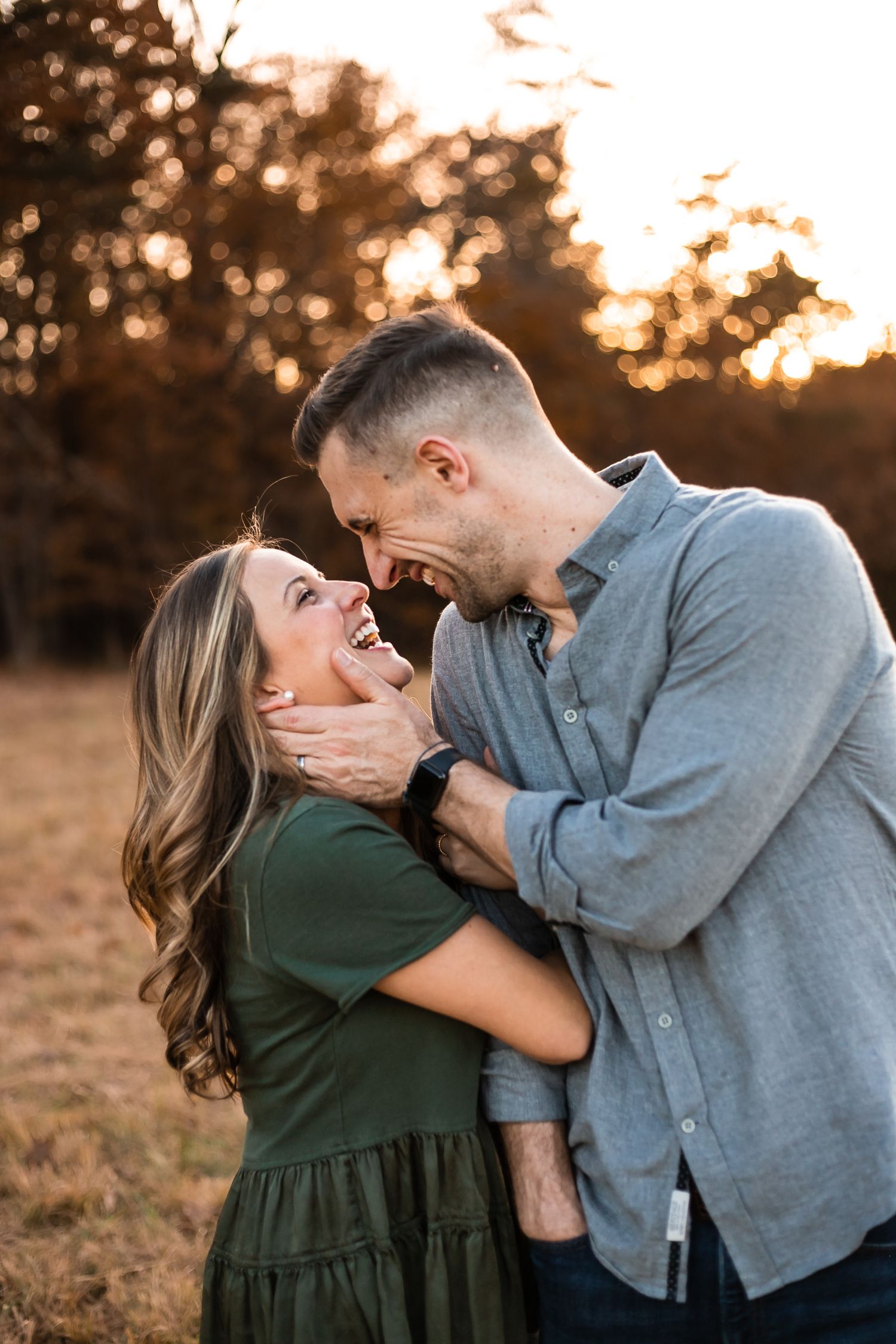 A couple shares an intimate laughing moment at sunset in a field with warm golden lighting.
