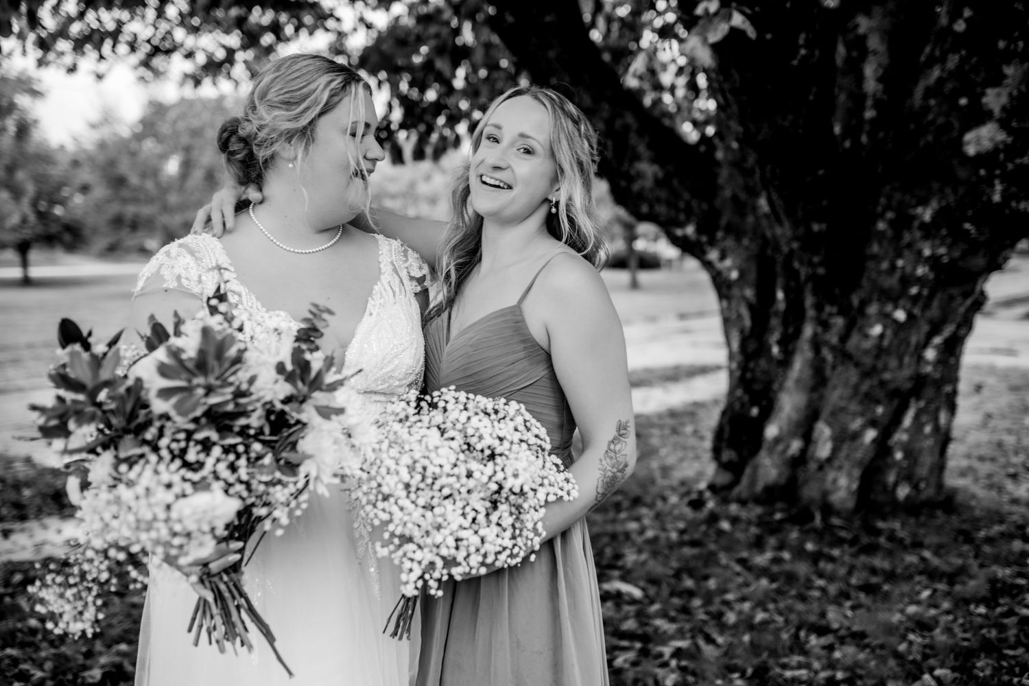 Two people in wedding attire share joyful laughter while holding bouquets of baby's breath flowers outdoors.