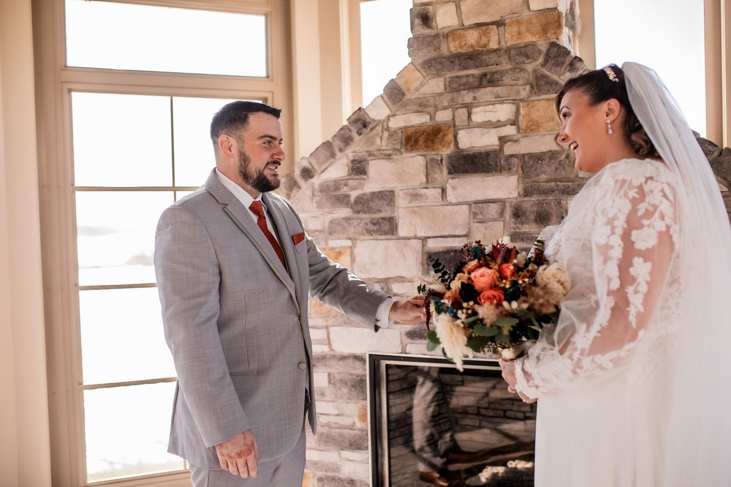Couple share emotional first look moment in front of stone fireplace.