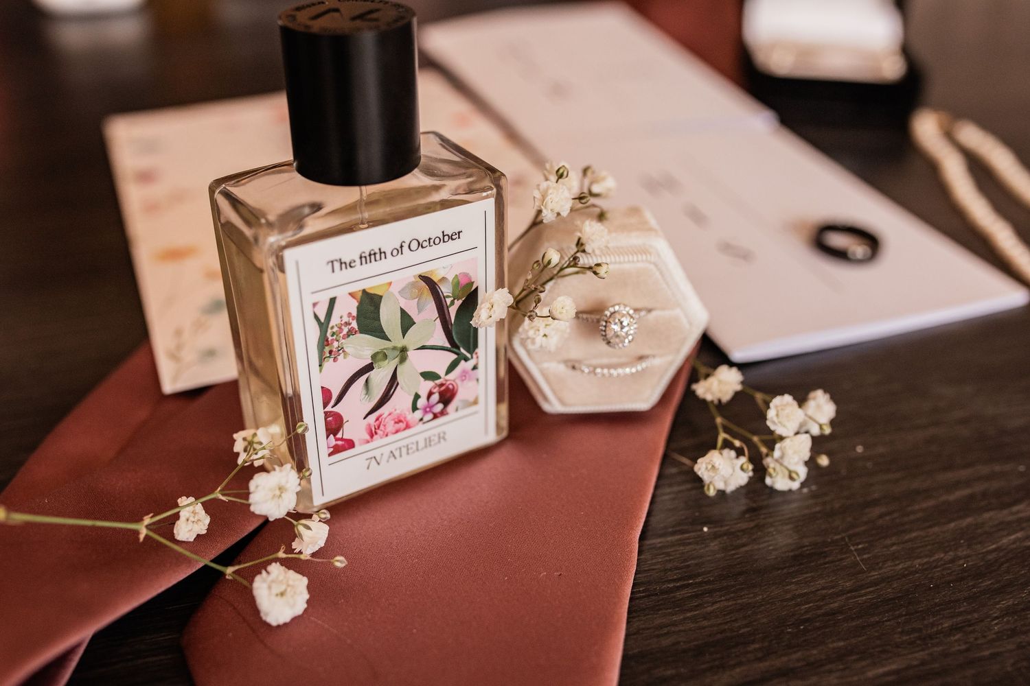 Wedding details including perfume bottle and delicate floral accessories on a burgundy surface.