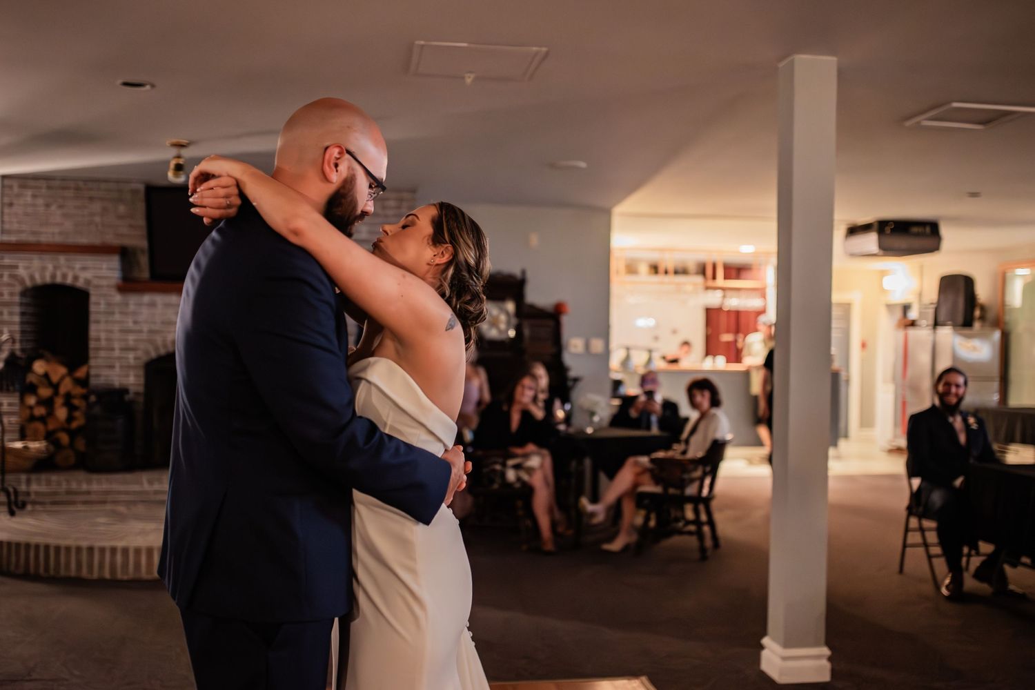 Couple shares first dance in reception venue with brick walls and indoor lighting.