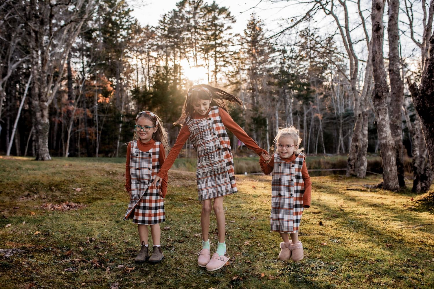 Group portrait of people in matching plaid flannel shirts standing in woods during sunset.