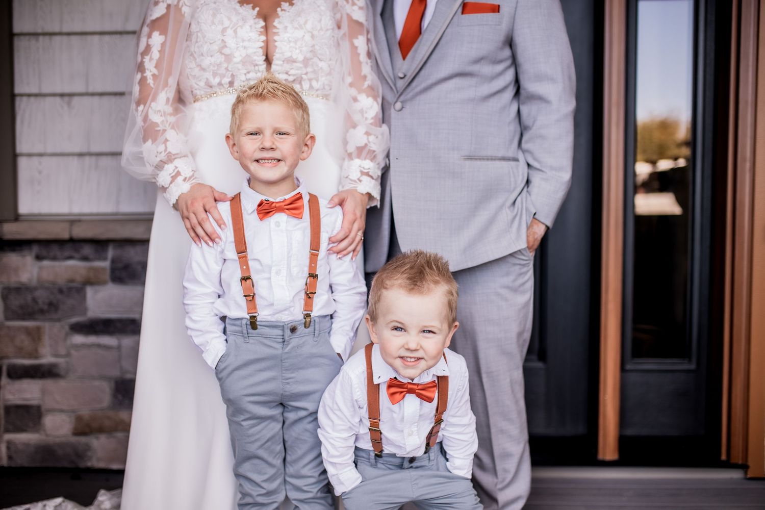 Two young ring bearers in suspenders and bow ties pose with wedding couple.