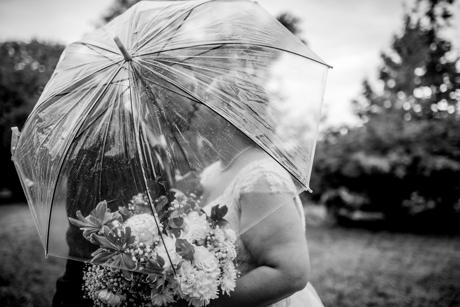 Clear umbrella shelters wedding bouquet in black and white artistic photograph.