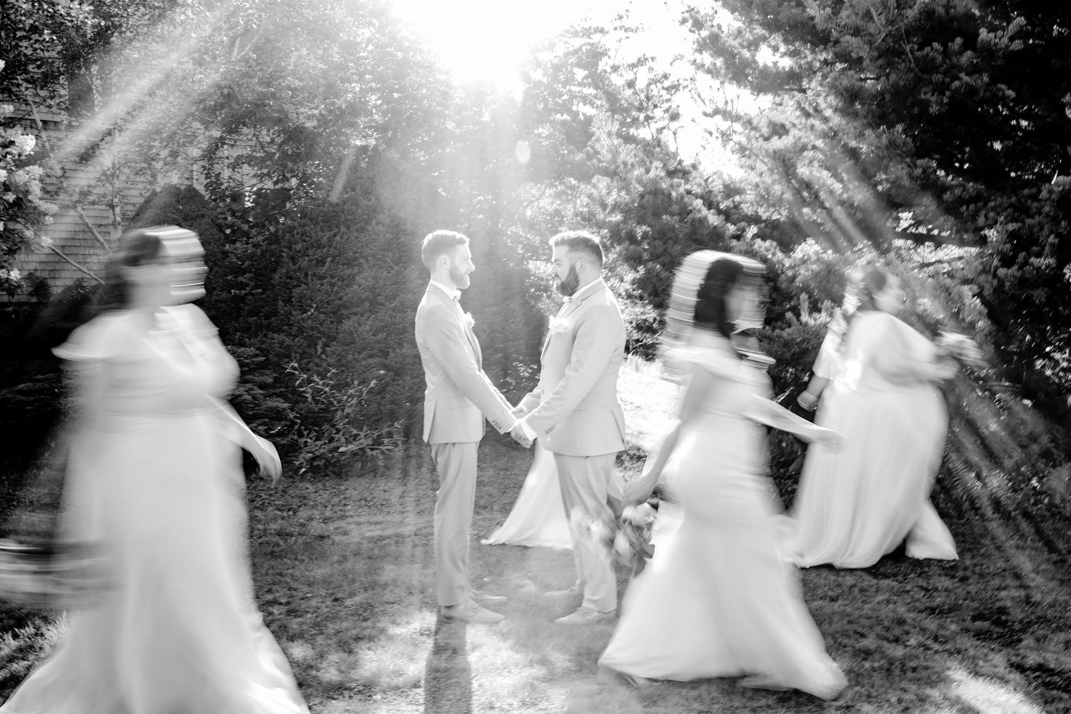 Artistic black and white photo of wedding party spinning in sunlit garden.