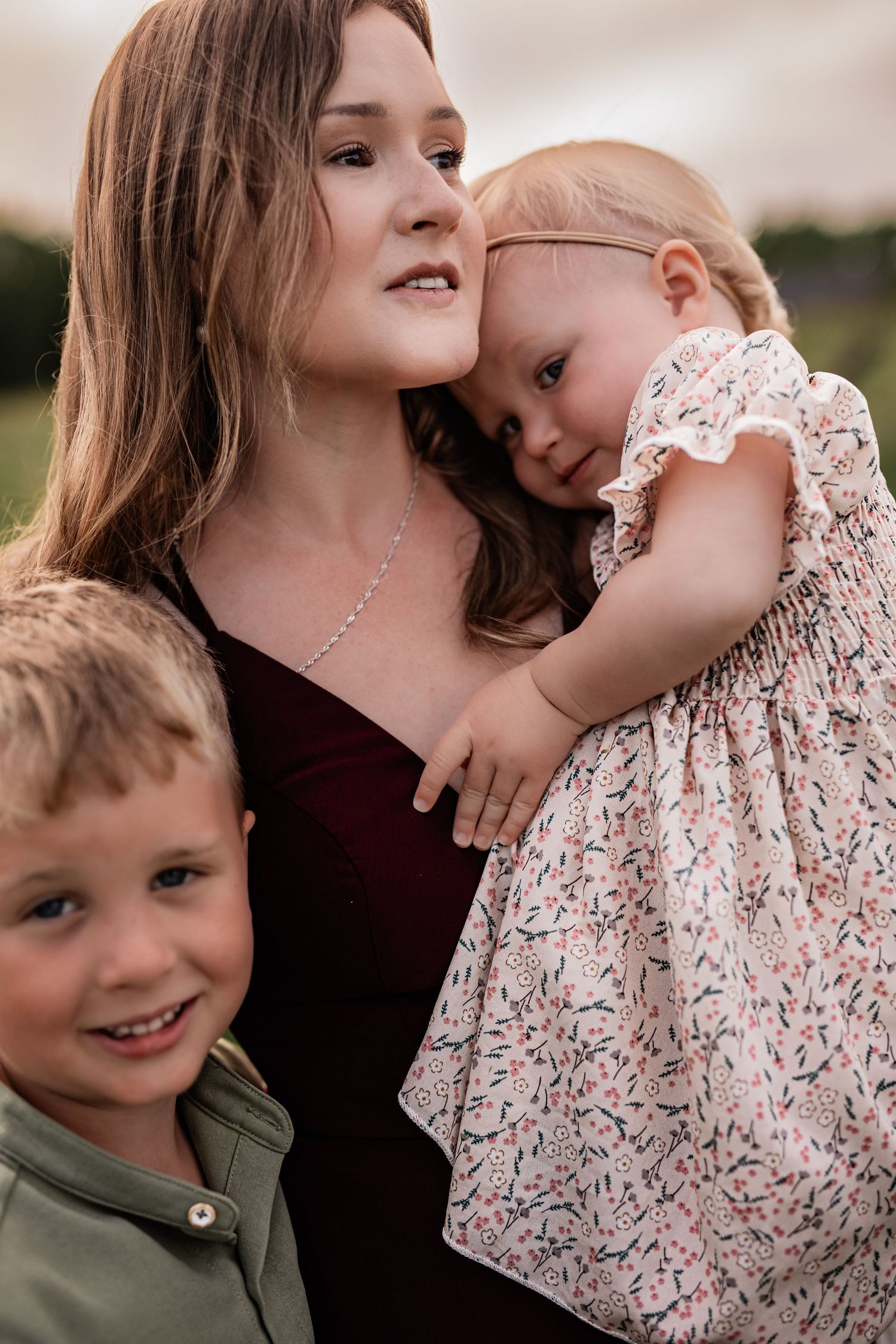 Candid family moments captured in a field with children wearing floral and olive green outfits.