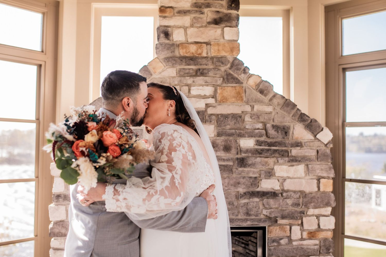 Couple sharing romantic kiss while holding floral bouquet by stone fireplace.