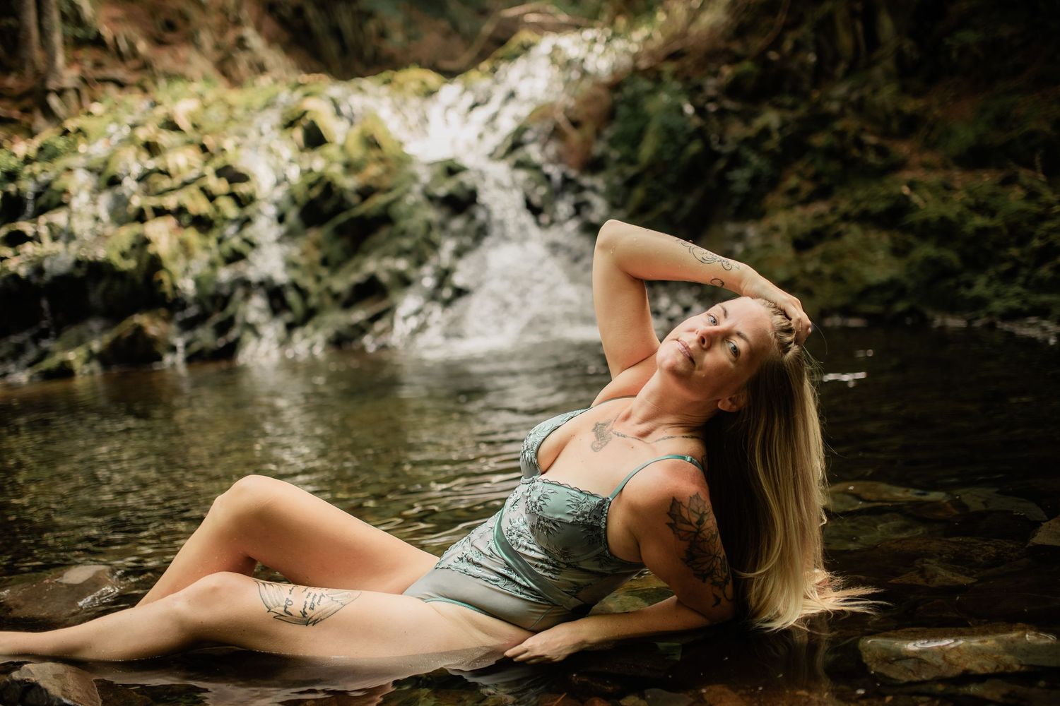 Artistic portrait at scenic waterfall with soft golden lighting and natural elements.