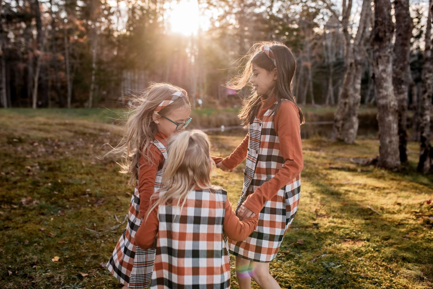 A family wearing coordinating plaid shirts poses together in a sunlit forest setting during golden hour.