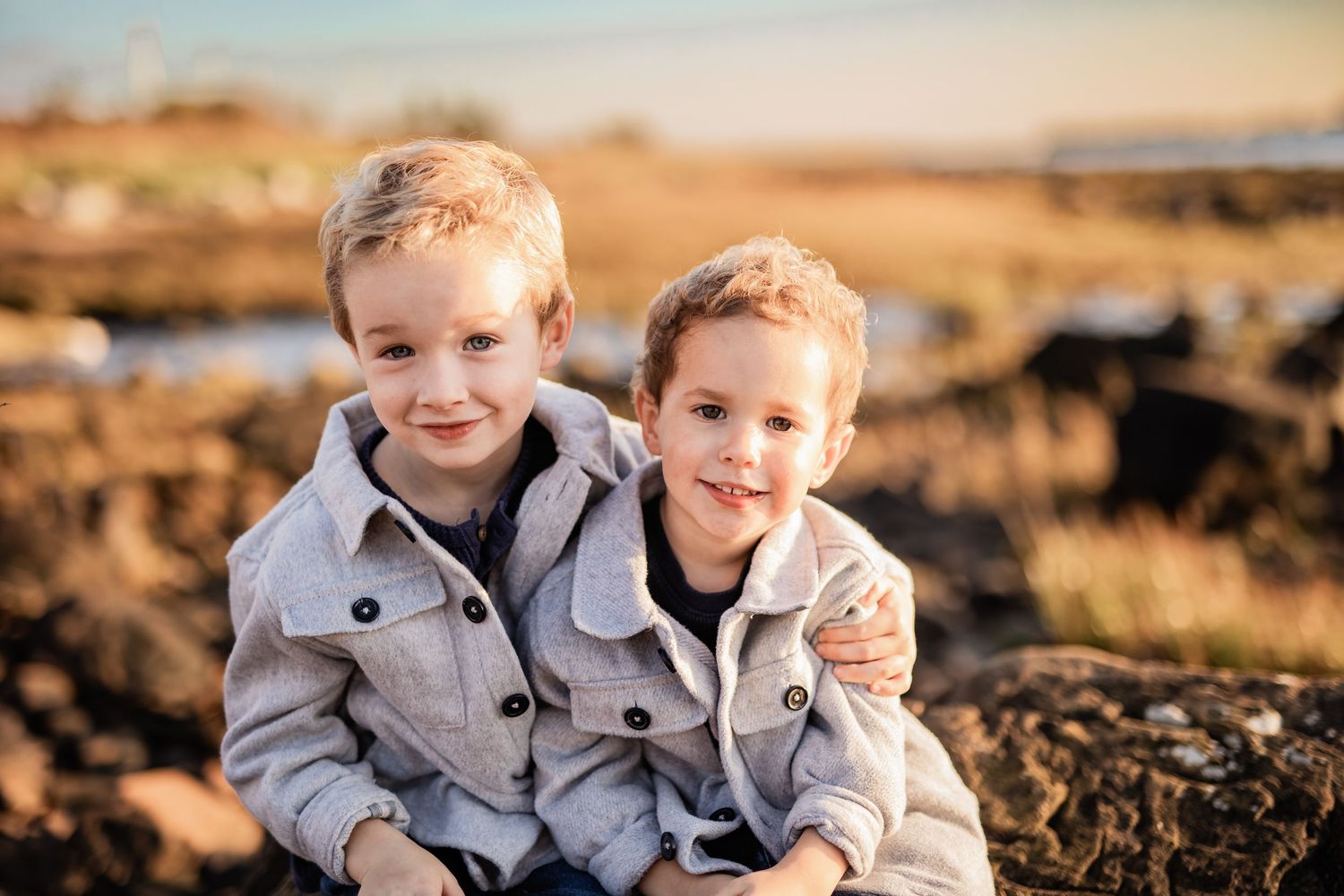 Two young siblings in matching gray outfits share joyful moments outdoors.