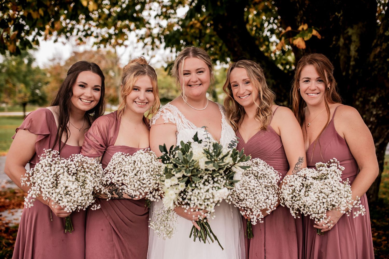 Wedding party in matching dusty rose dresses holding baby's breath bouquets.
