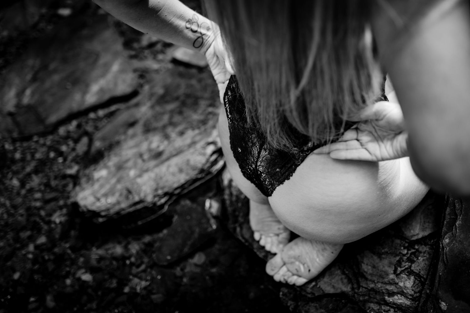 Close up black and white detail shot of bare feet on wet dark rocks.