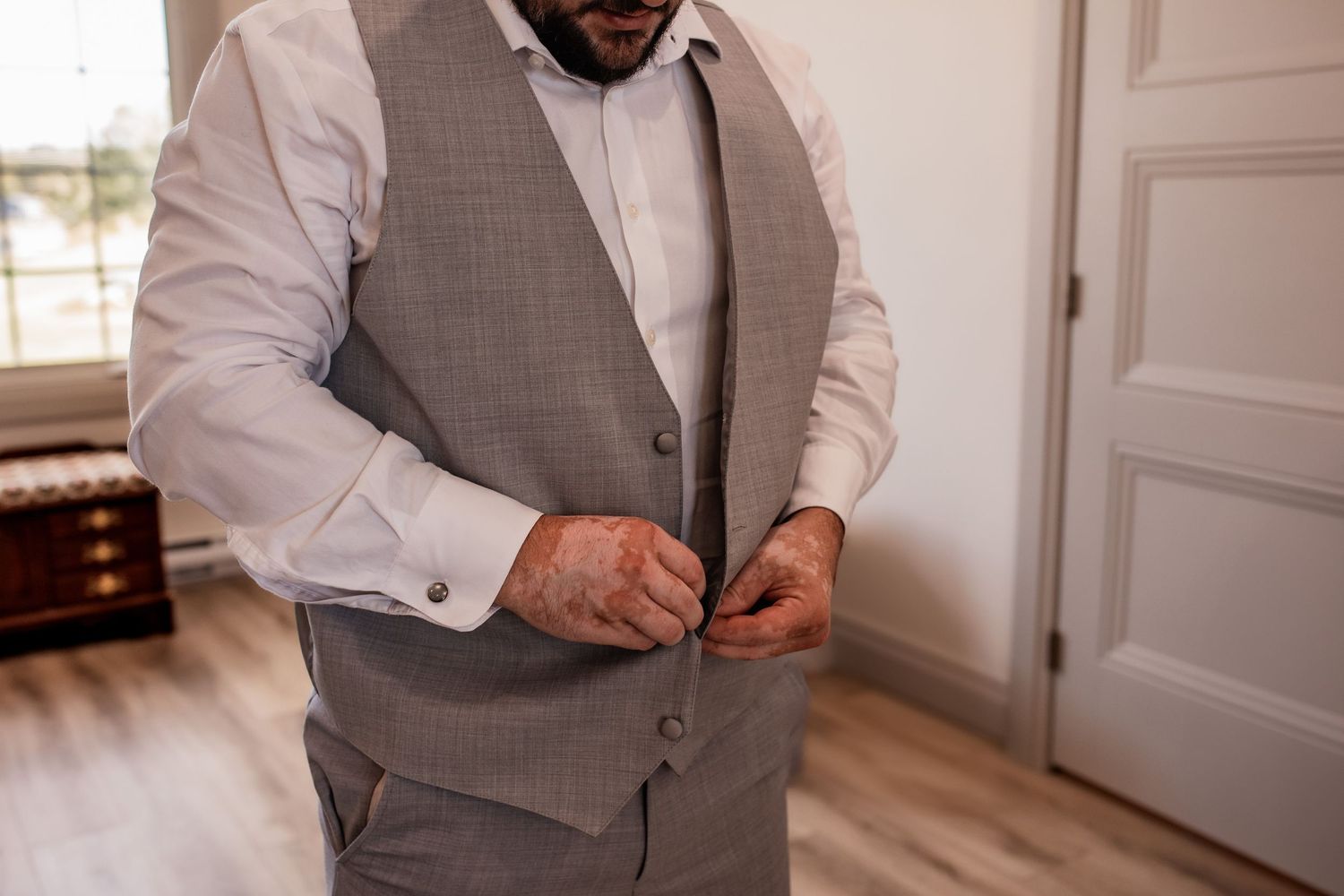 Person adjusting buttons on light gray vest while getting ready.