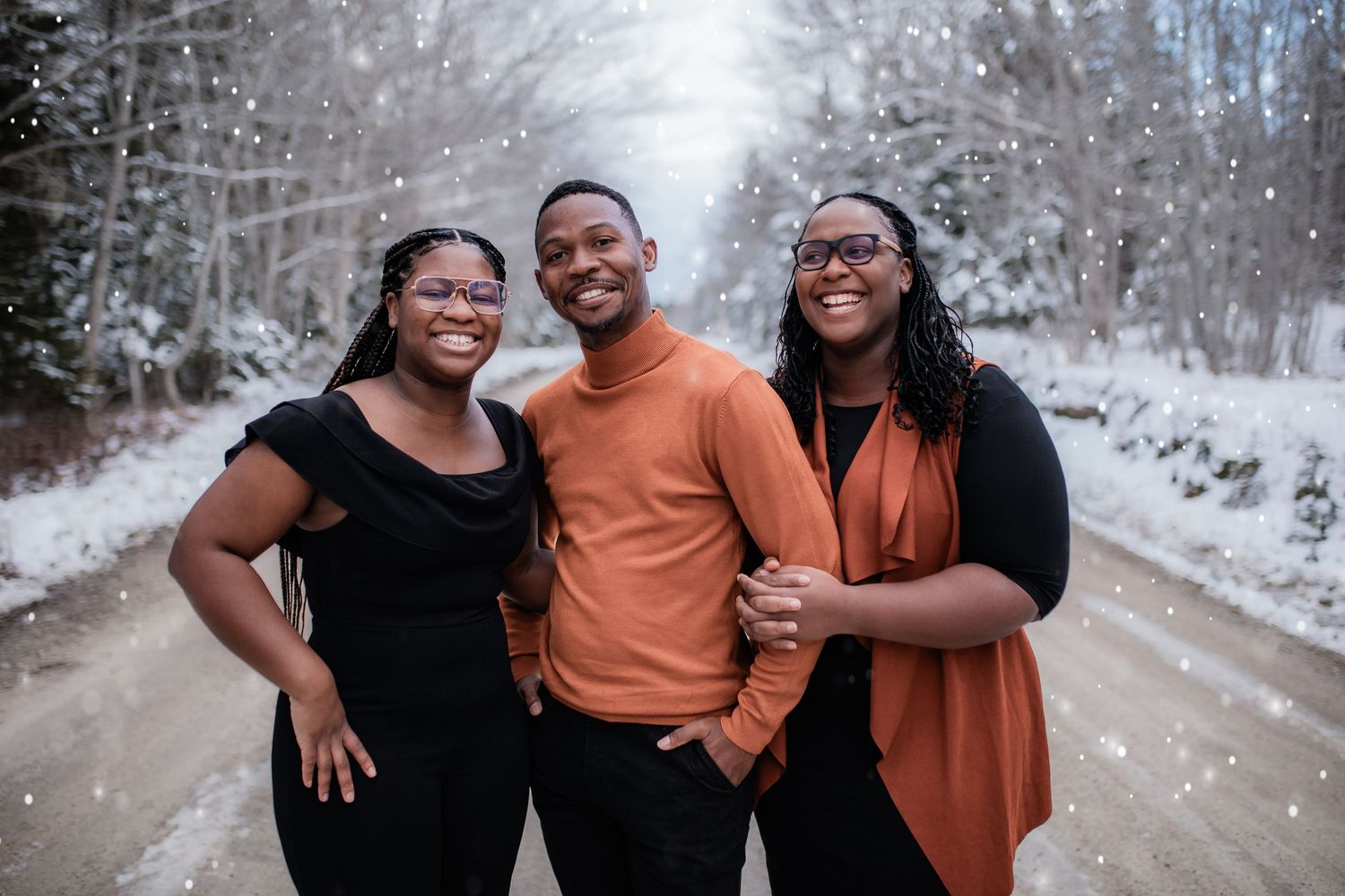 Three people posing together on a snowy winter road with falling snowflakes.