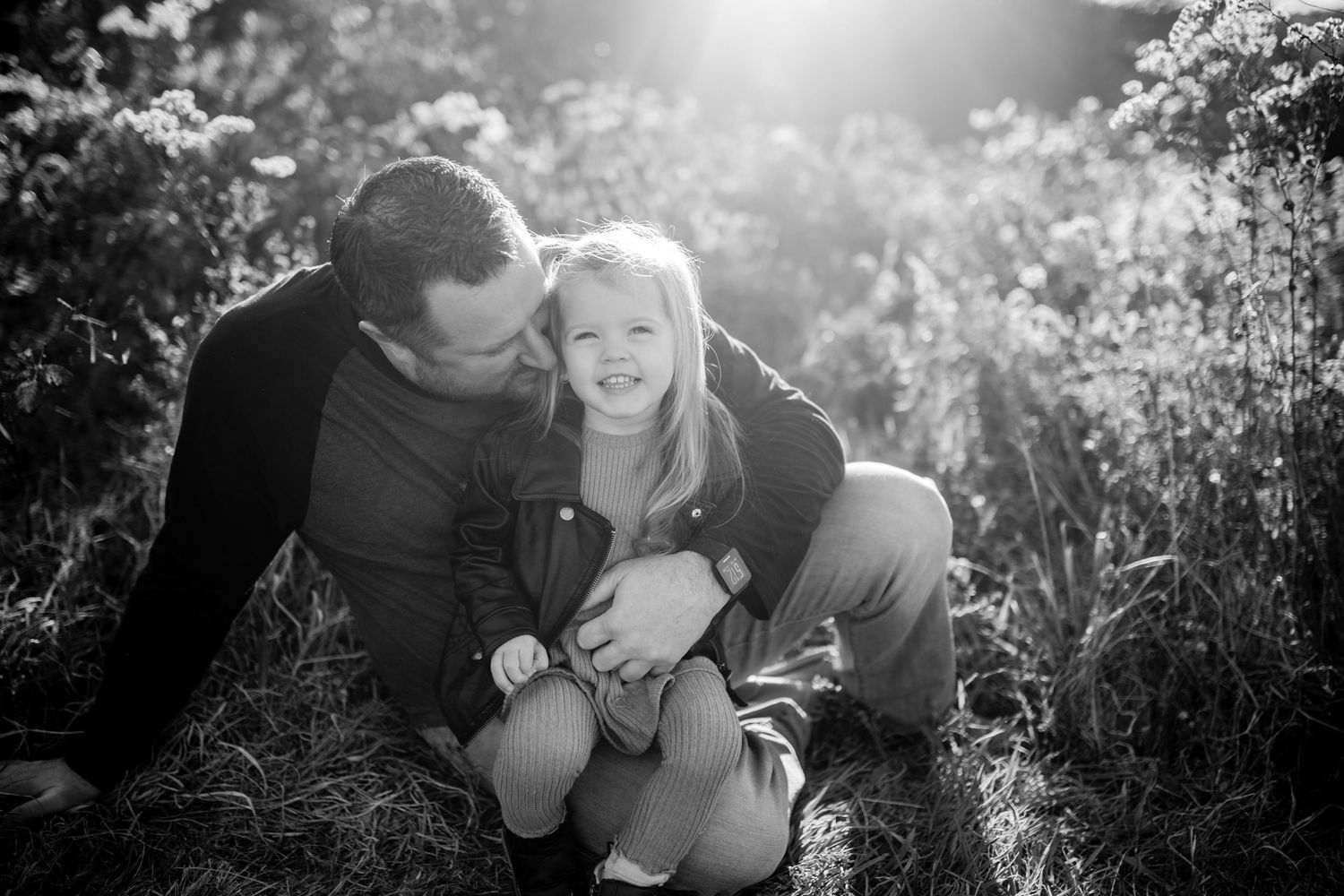 A black and white photo capturing playful interaction in an outdoor setting with sunlight streaming through.