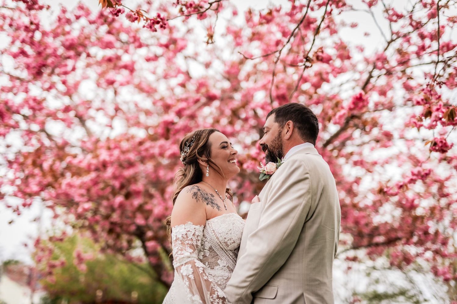 A romantic wedding portrait under vibrant pink cherry blossom trees in bloom.