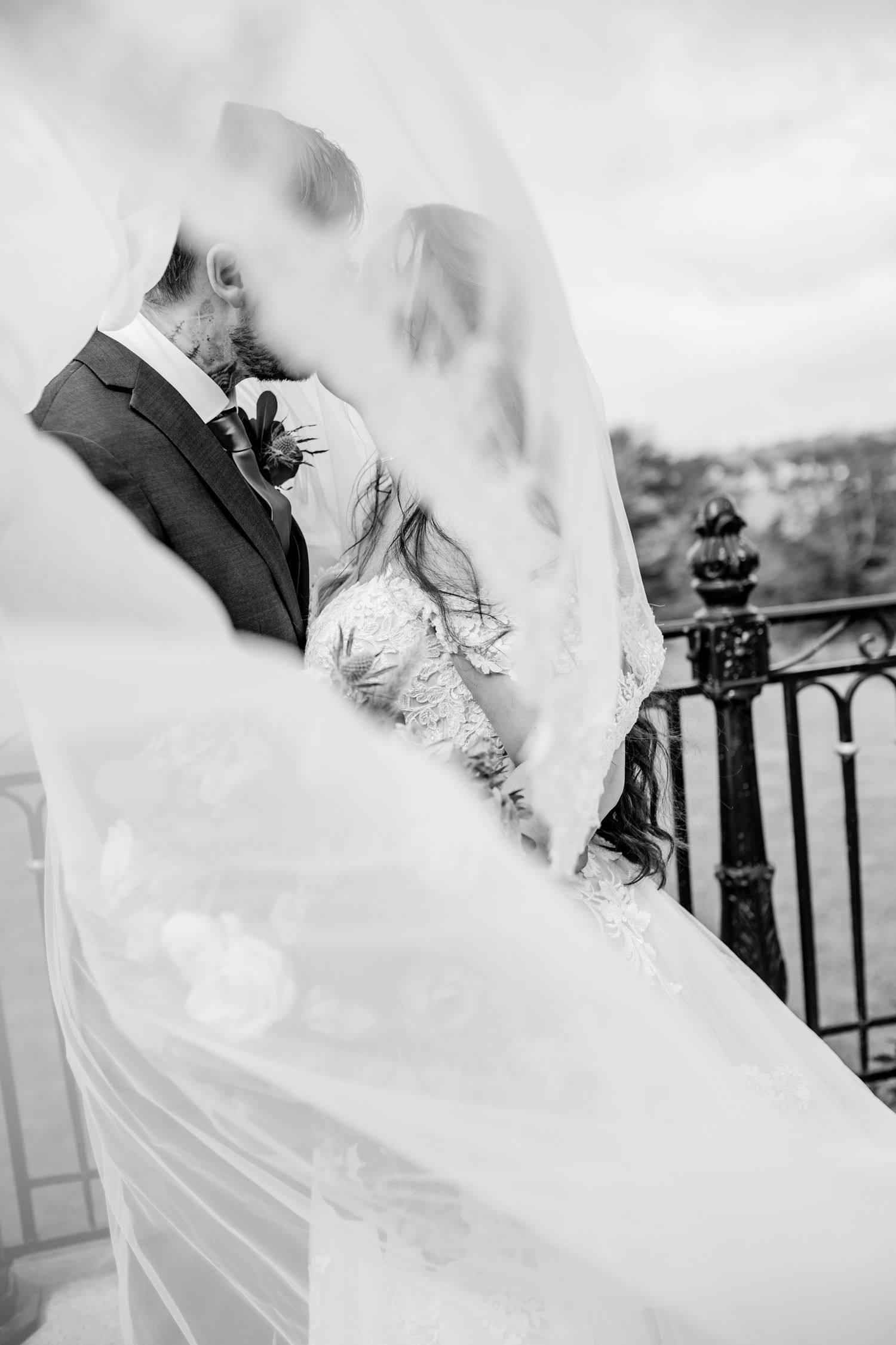 Artistic black and white wedding photo with couple kissing under flowing veil.