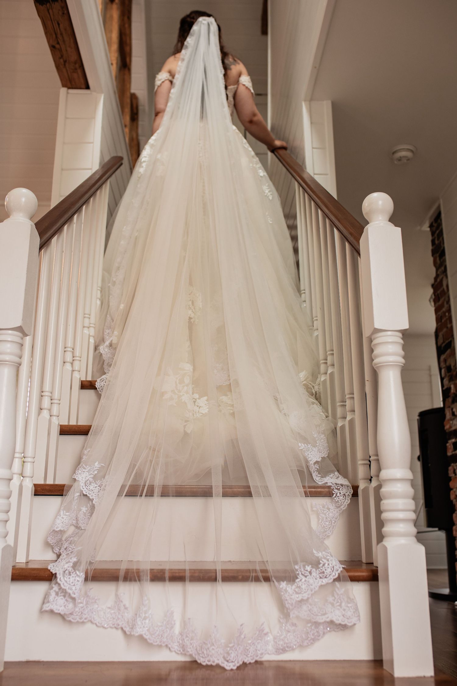 Long lace wedding veil trailing down white wooden staircase in elegant indoor setting.